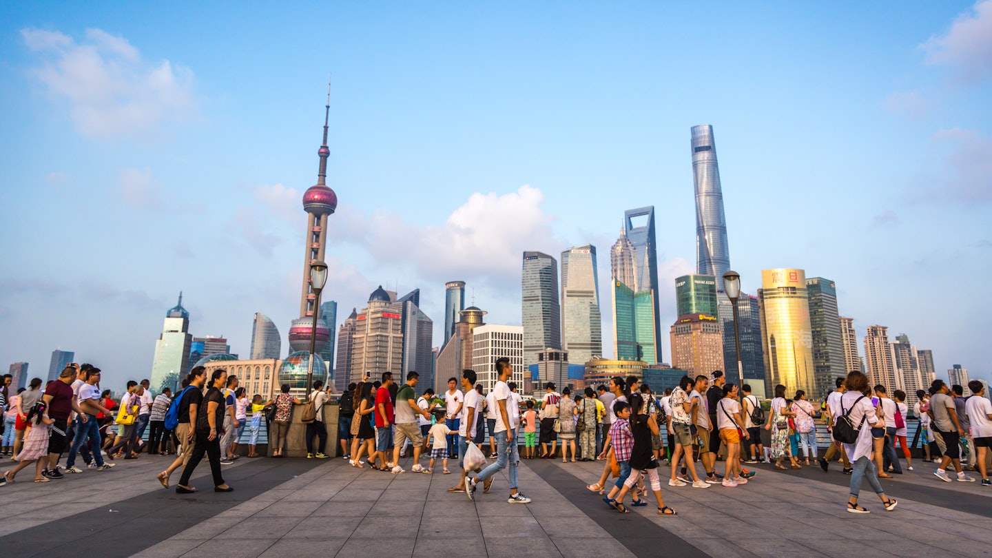 Pedestrians walking along the west bank of the Huangpi River in Shanghai, with views of skyscrapers in Pudong.