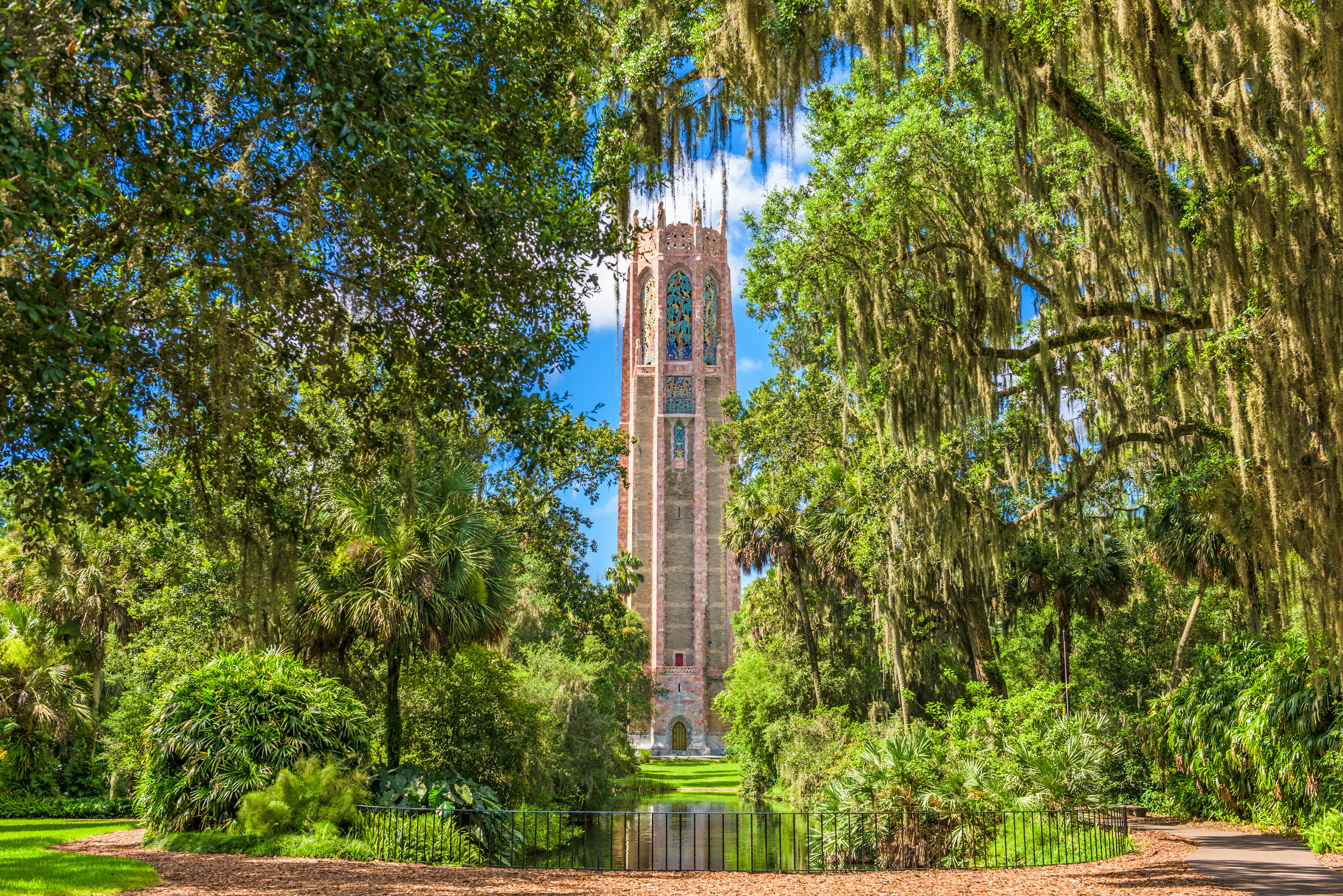An ornate, tall tower rises among lush trees in a landscaped garden.