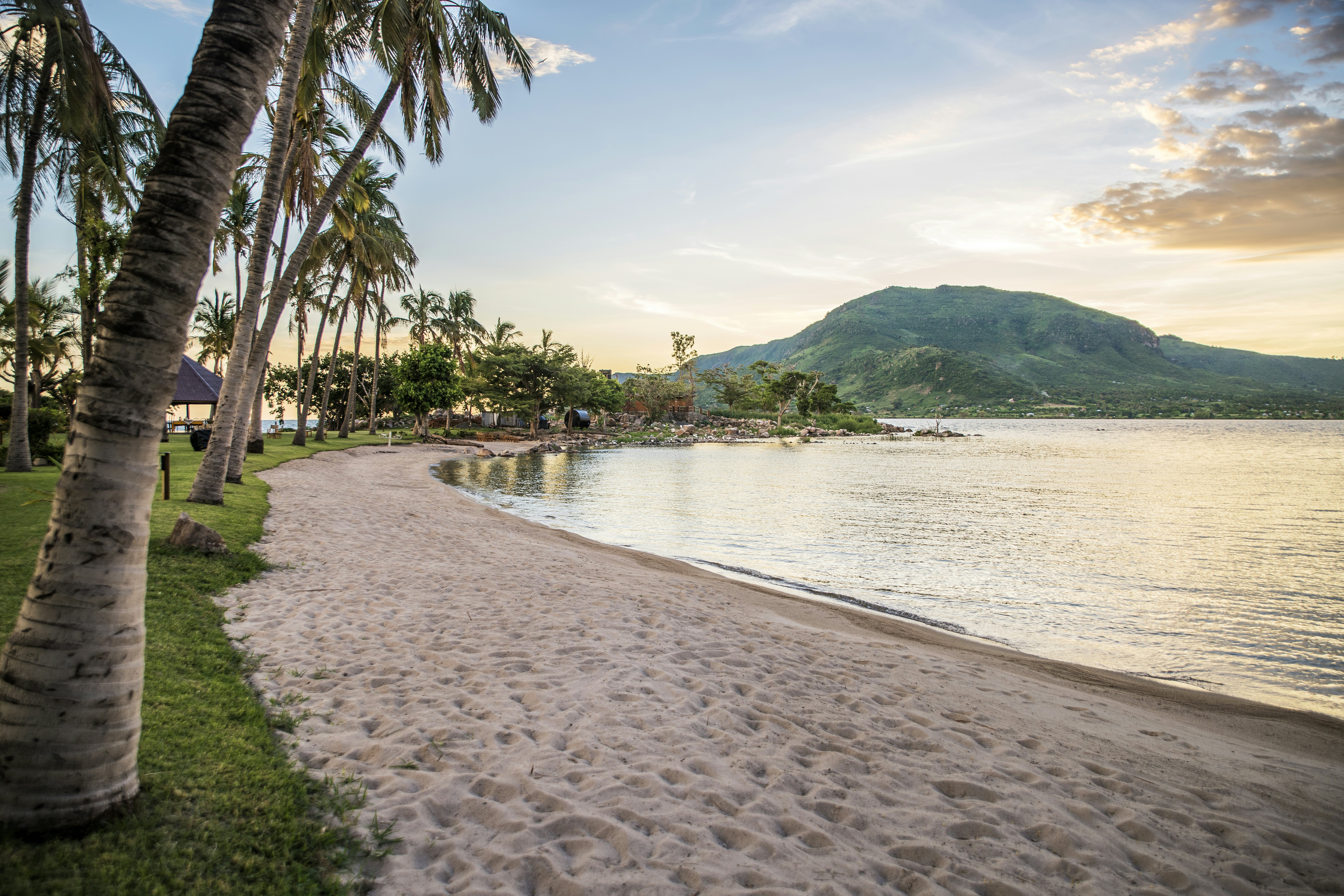 A pink-tinged sandy beach on shores of a lake in Kenya, with a mountain in the background.