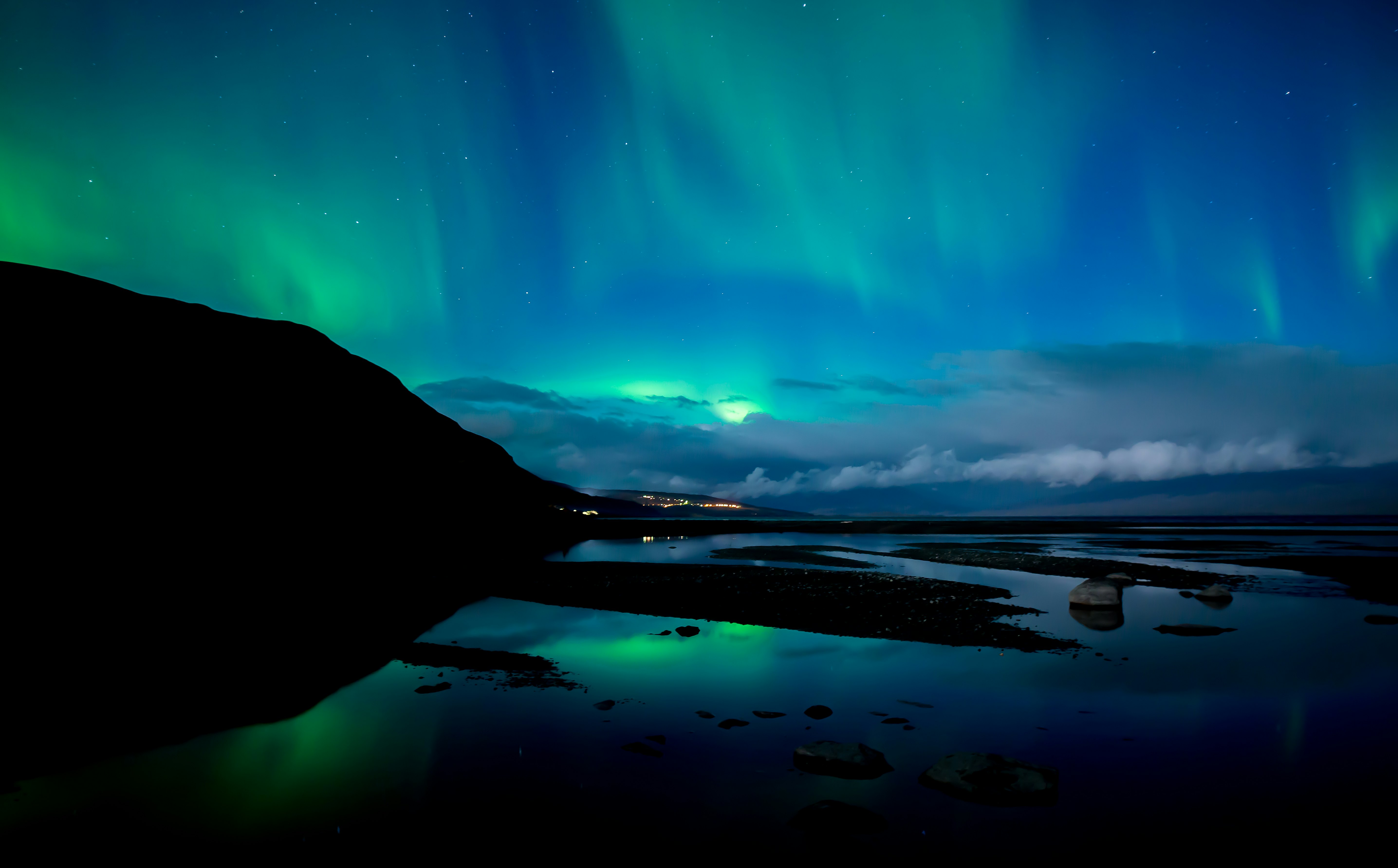 The aurora borealis color the night sky green above a lake and mountains.