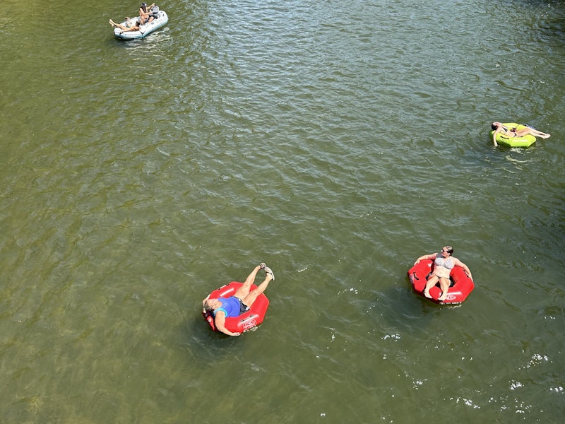 Swimmers in bright red tubes floating along the green Boise river