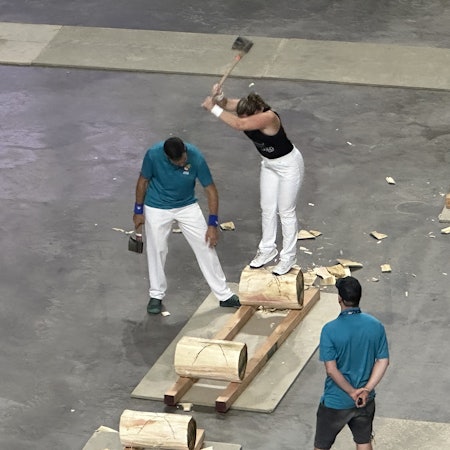 Woman using axe to chop log she is standing on