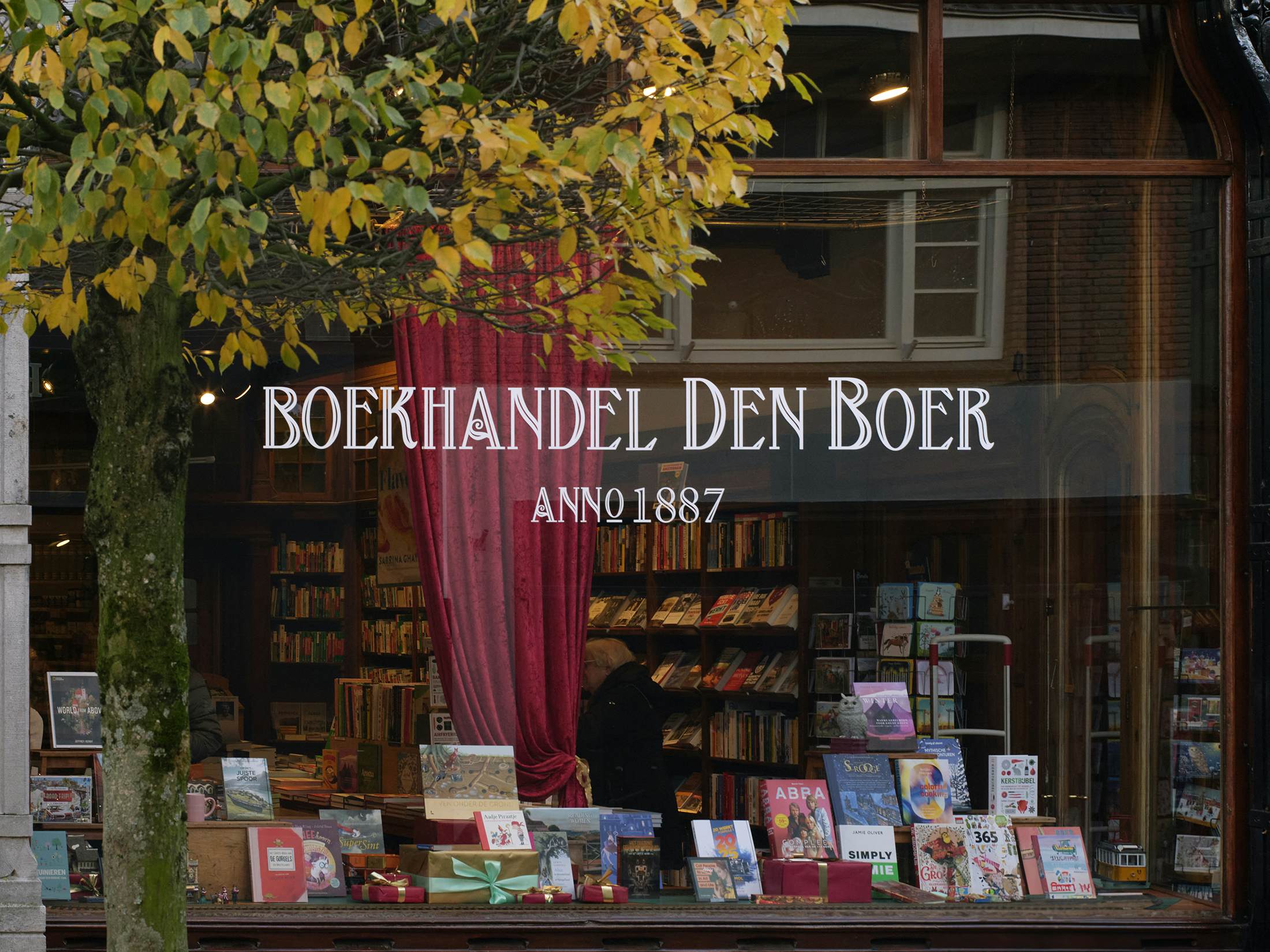 The window of a bookstore. A red curtain is draped across the window, partially blocking the view of the floor to ceiling bookshelves.