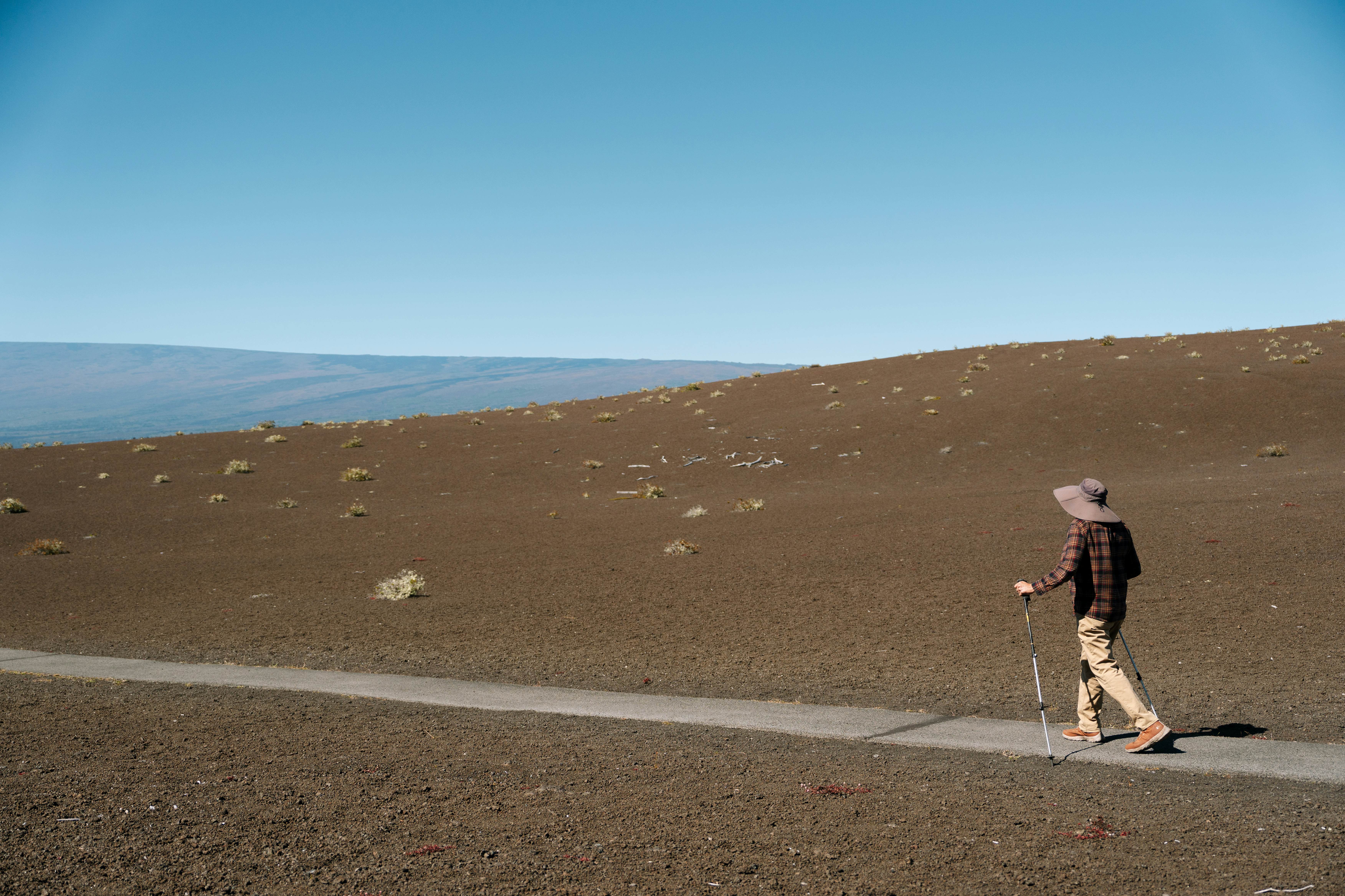 A hiker walks on a path through a barren landscape in Hawai‘i.