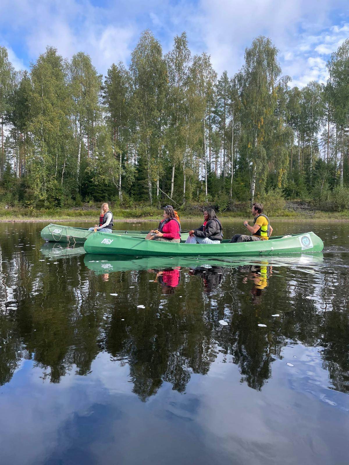 Four people canoeing in the forest while riding a green canoe