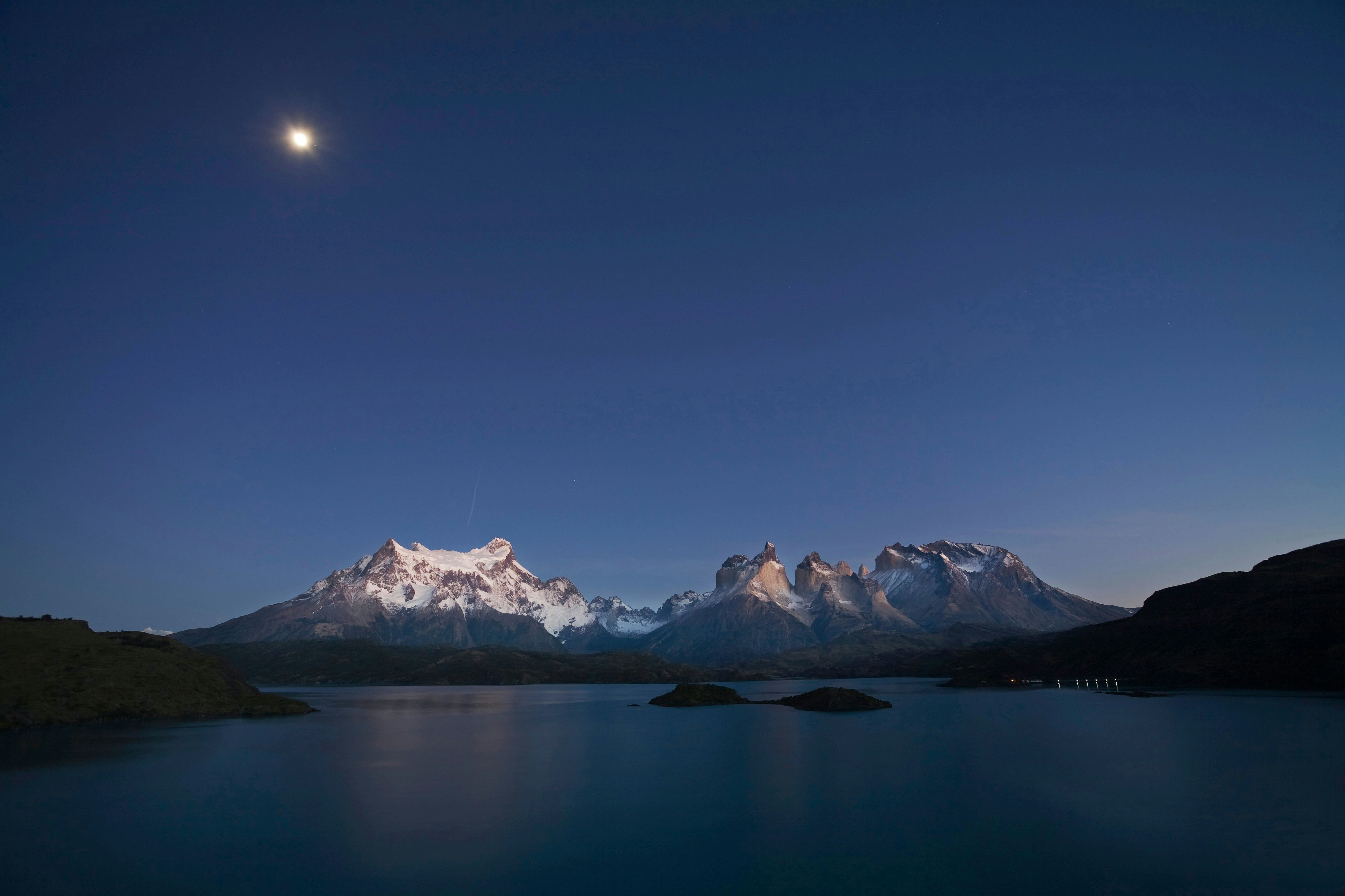 Dawn hitting snow-topped mountains that overlook a clear and glassy lake