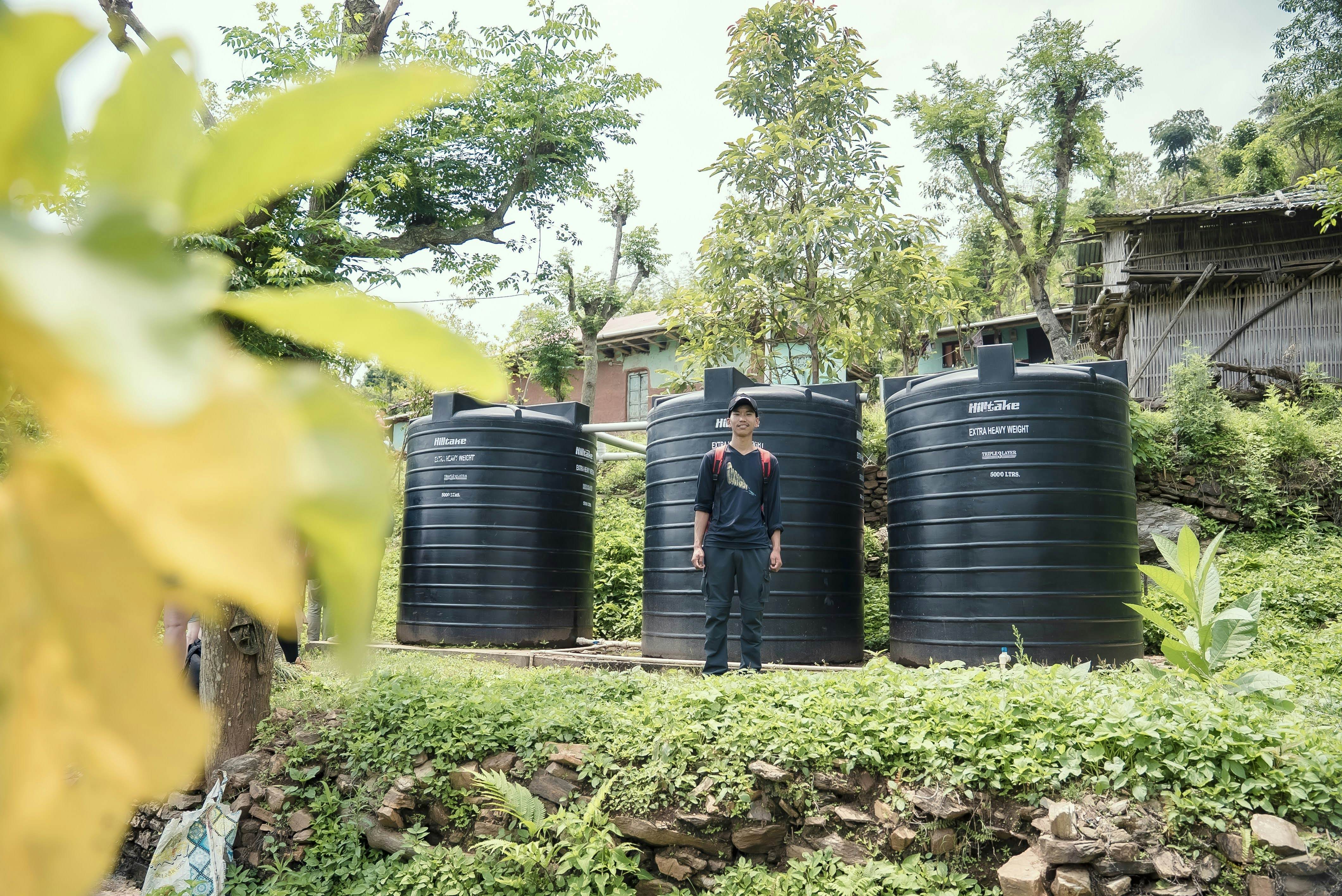 A Nepali man stands in front of rainwater harvesting tanks.
