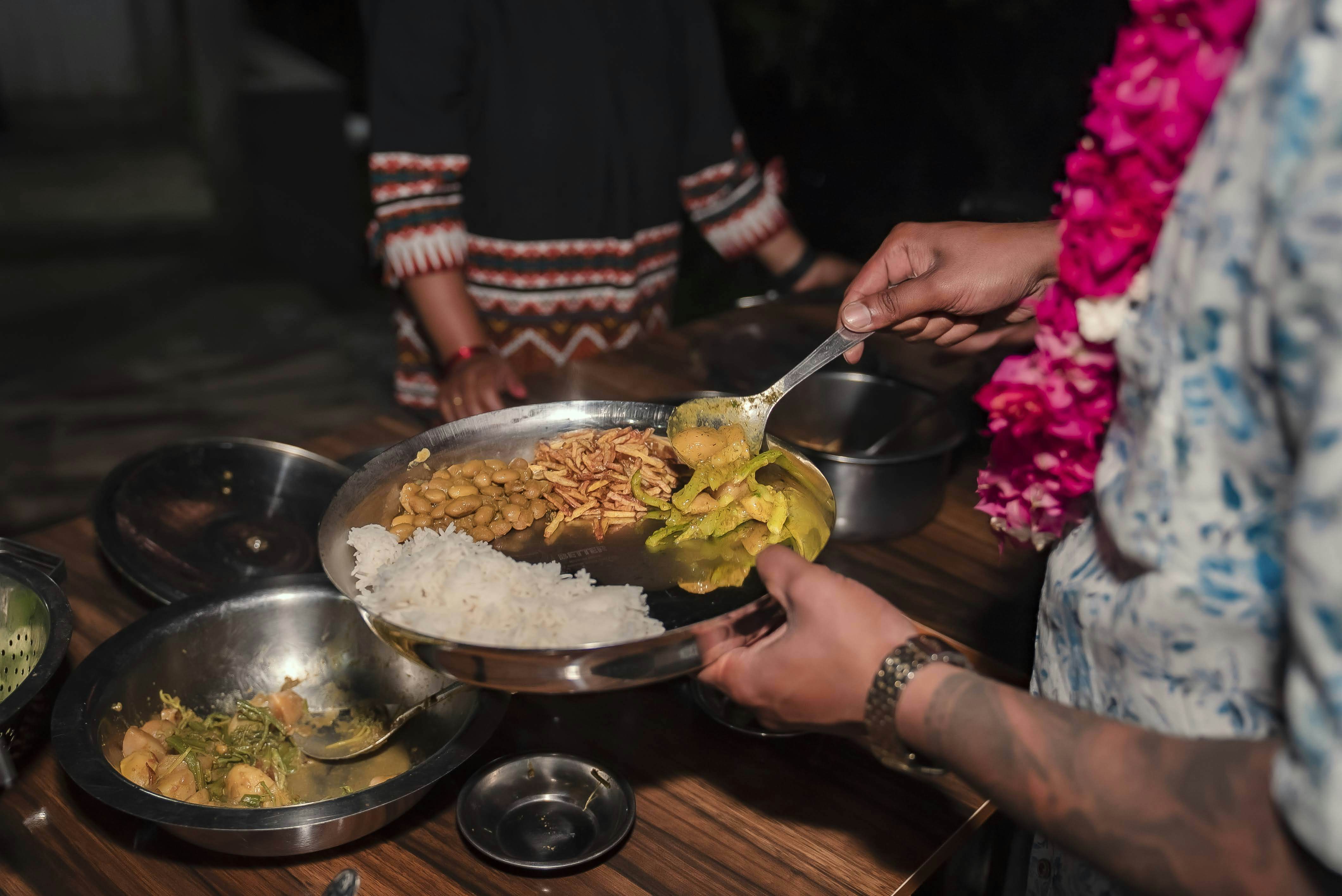A hand holding a metal dish with rice; they are spooning in additional food items.
