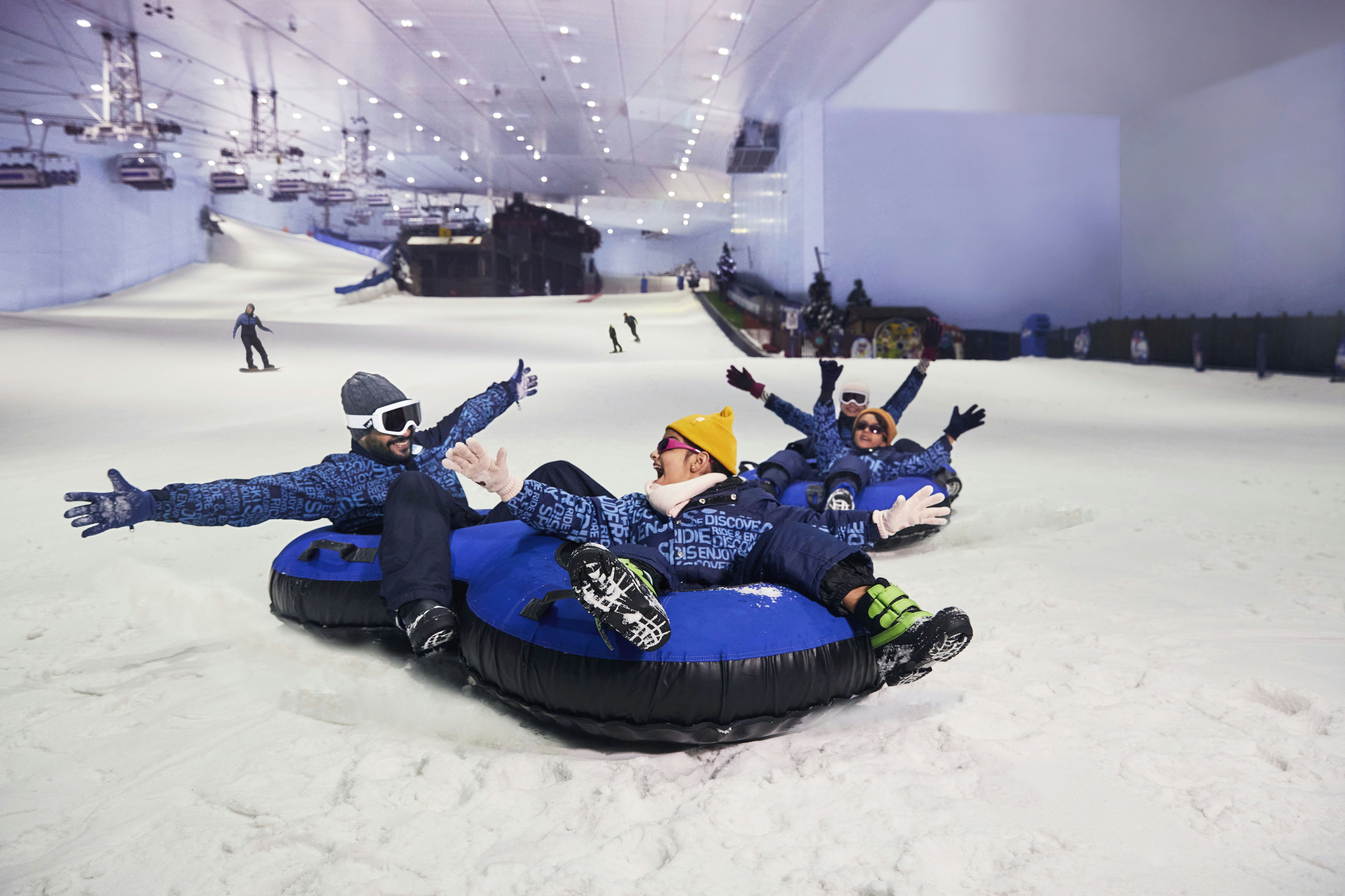 Four people riding sleds down an indoor snowy mountain.