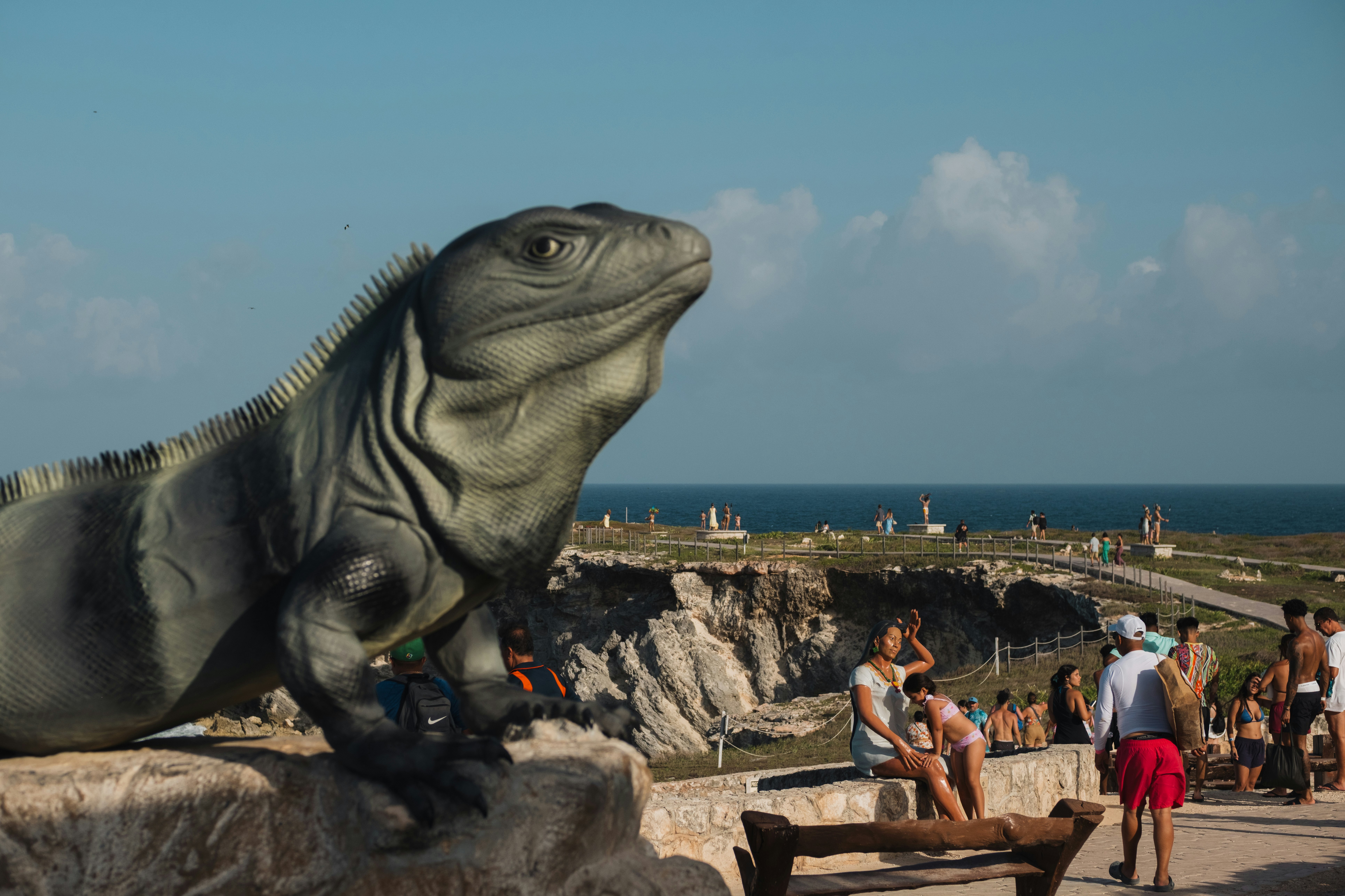 An iquana statue on a cliffside pathway surrounded by other statues and people