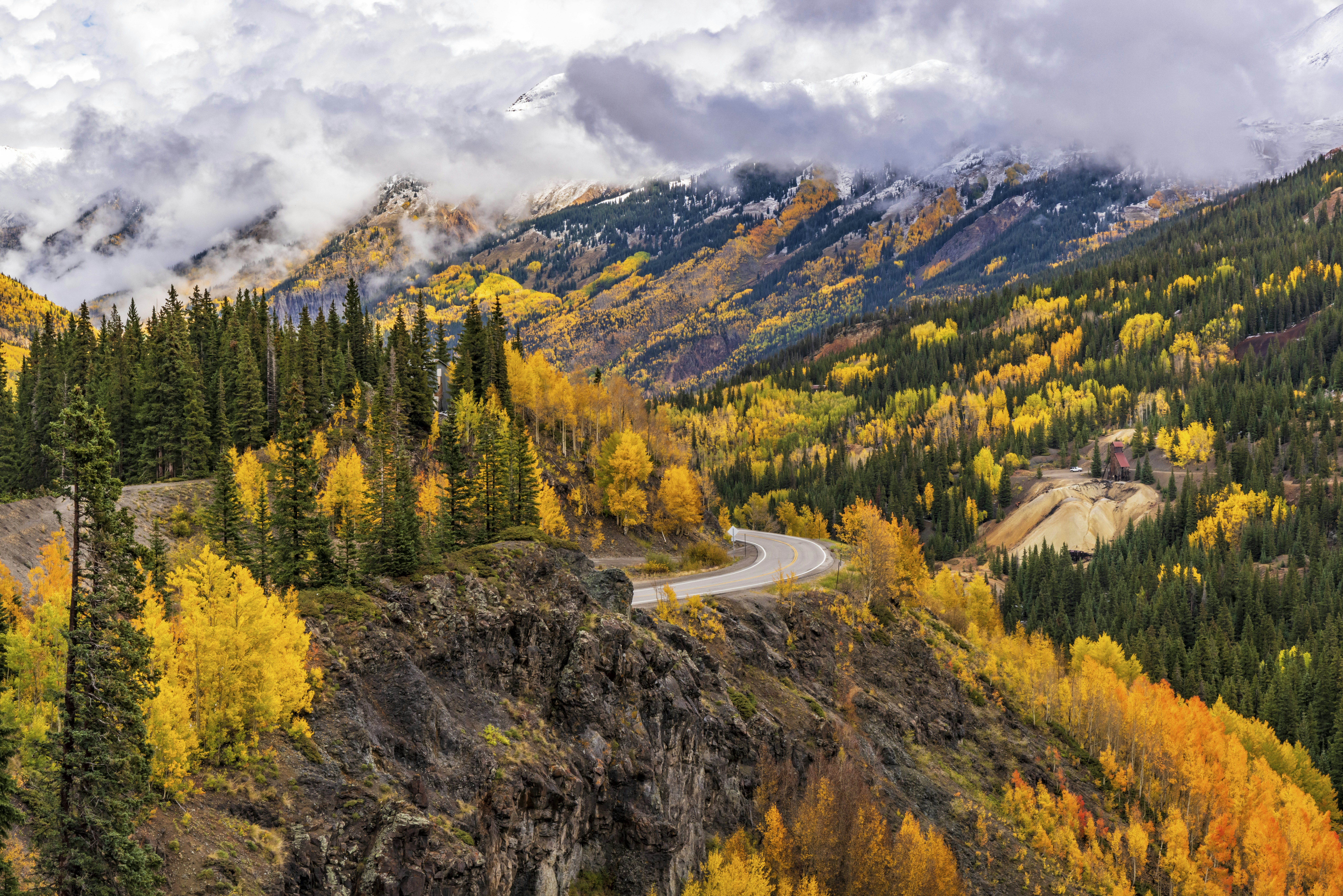 A road winds its way through mountains covered in trees colored yellow and green in autumn.