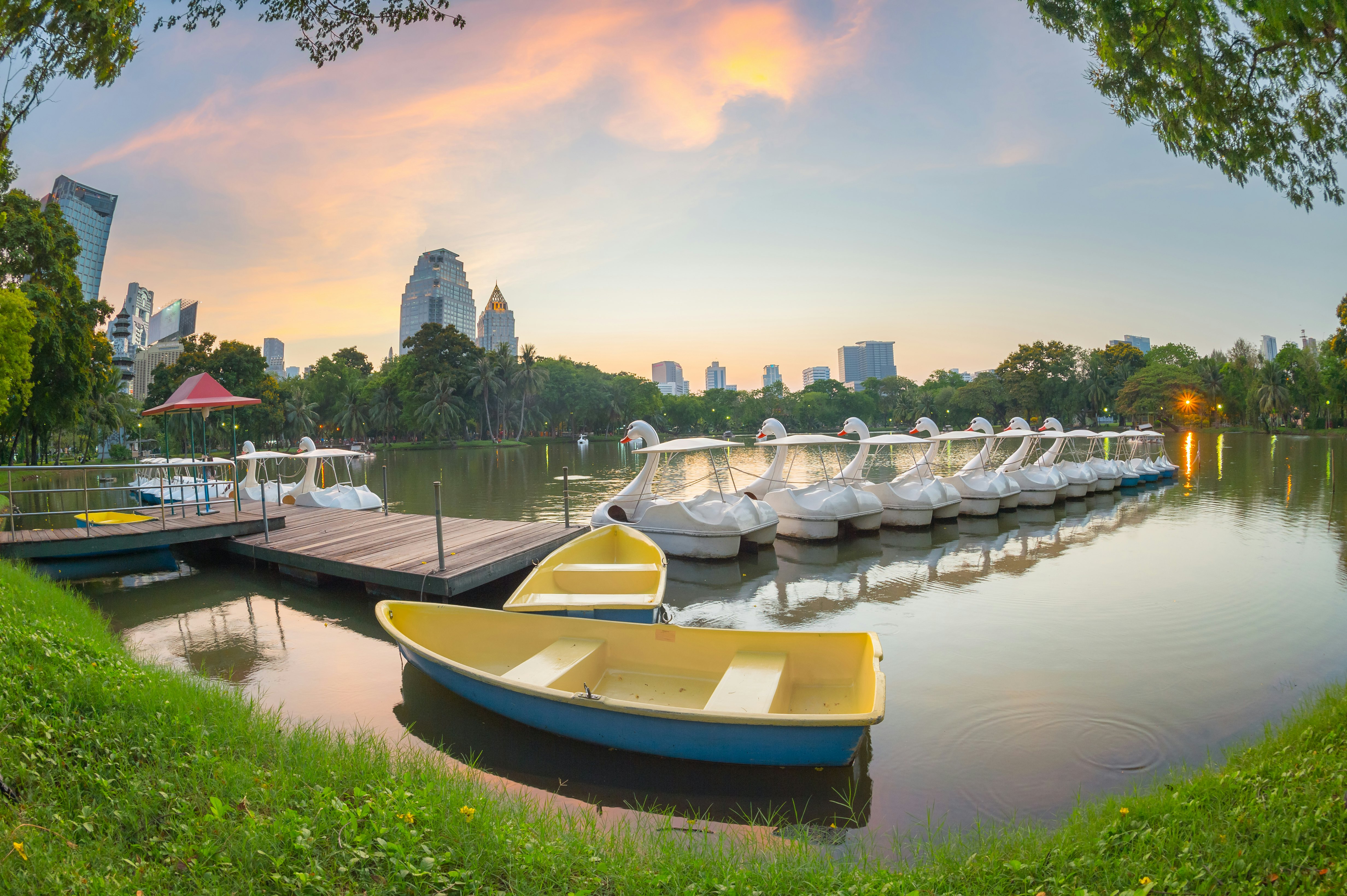 A line of white swan-shaped boats on a dock, with two small blue and yellow rowboats in the foreground