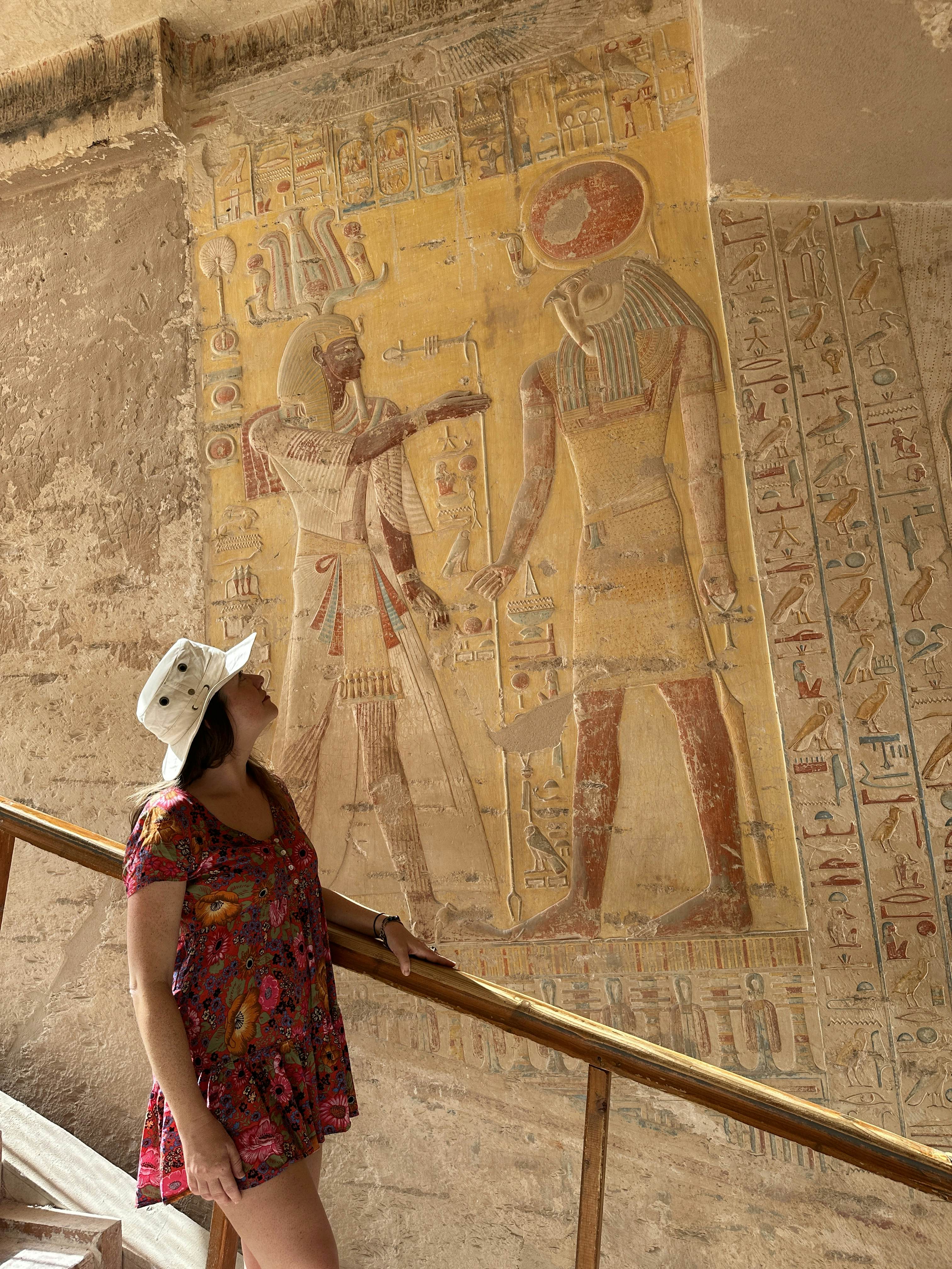 Woman in a red dress and a white hat looks at ancient Egyptian art