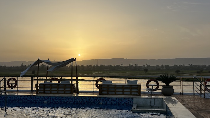 A pool lined with large couches in front of a river of water