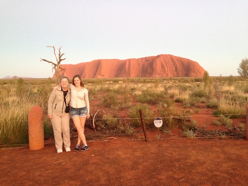 Two women smiling and laughing for the camera with Uluru rock in the background