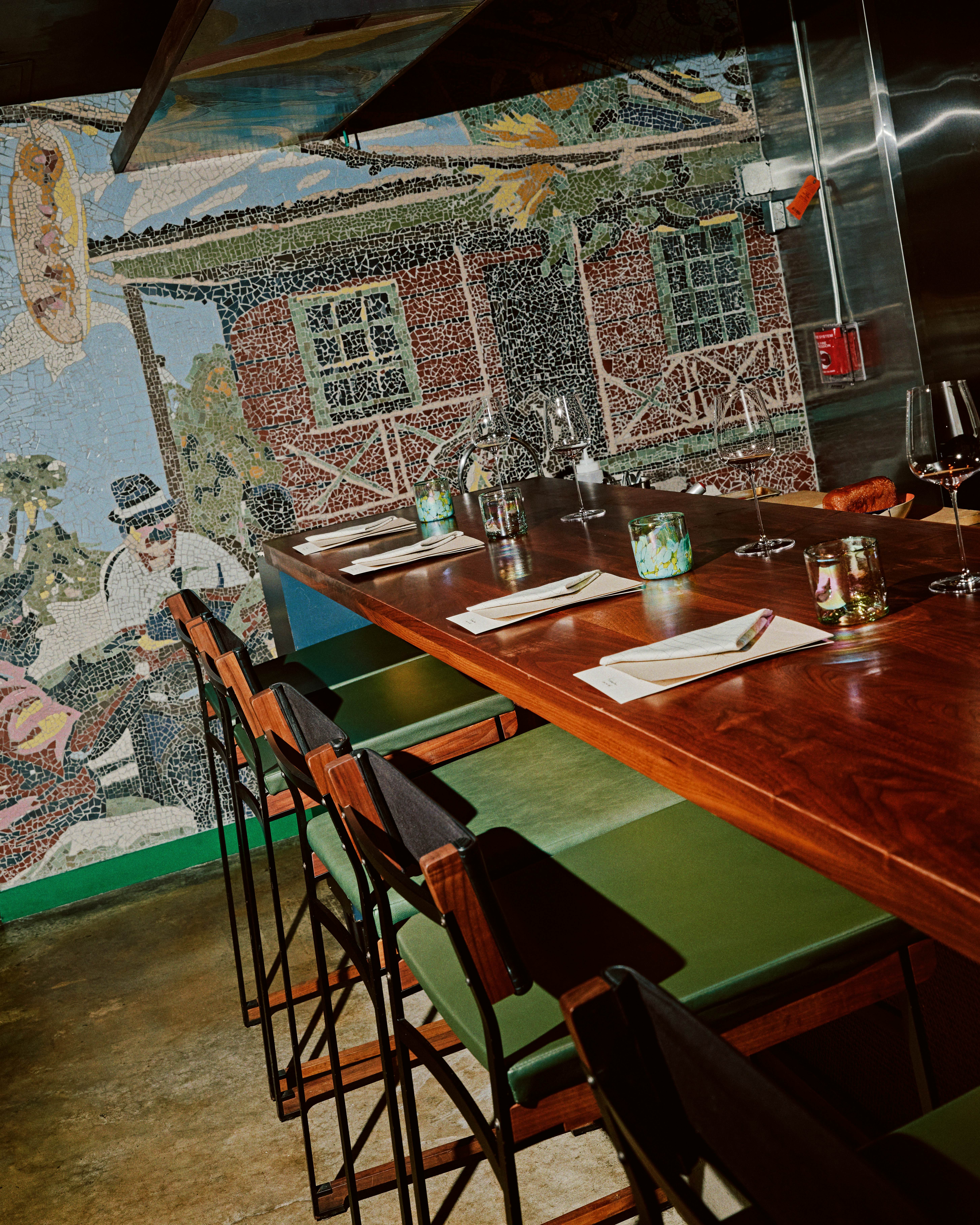 Green and wood bar stools are tucked under a wooden bar set with napkins. 