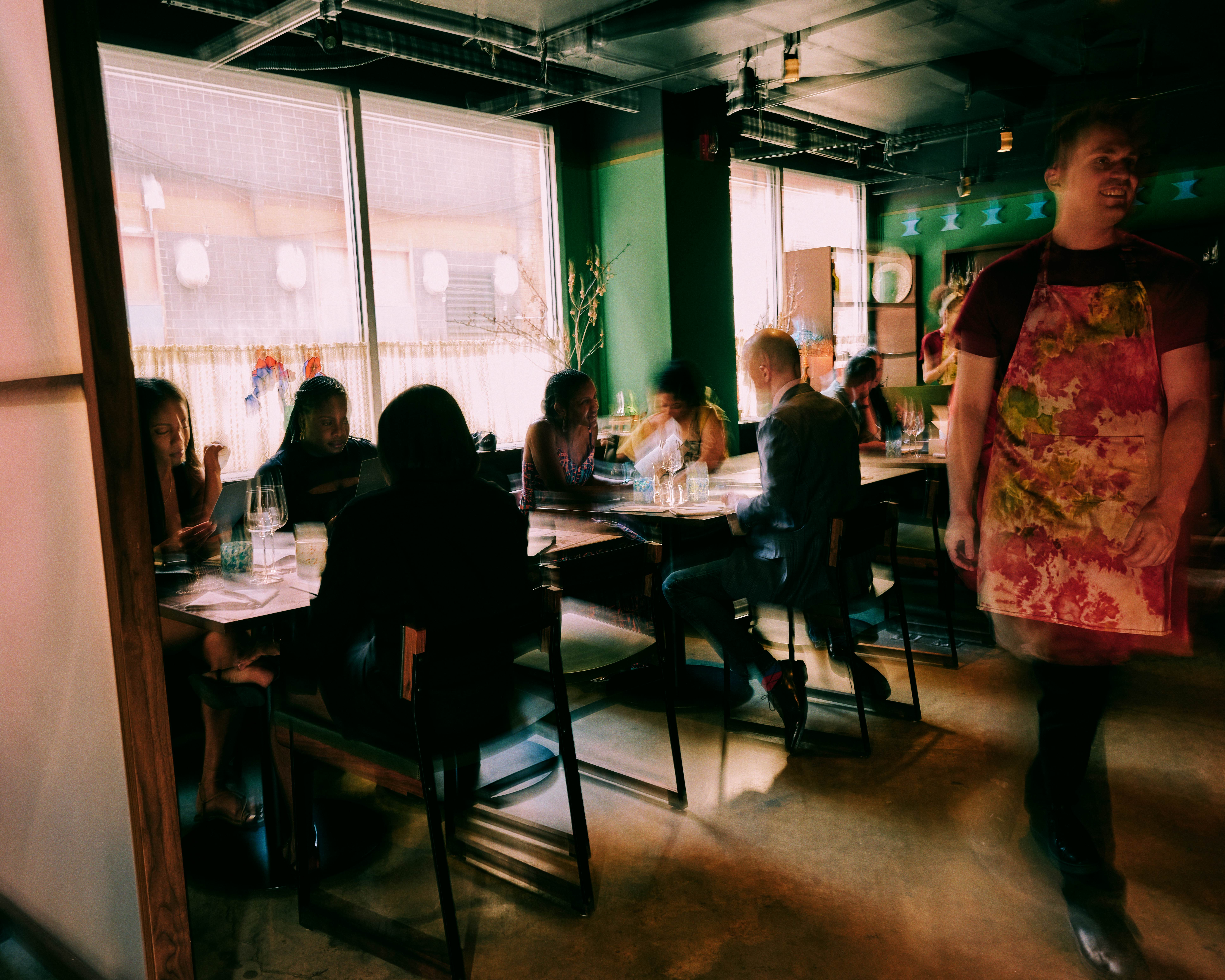 Blurred diners eat at tables against a window at a New York City restaurant.