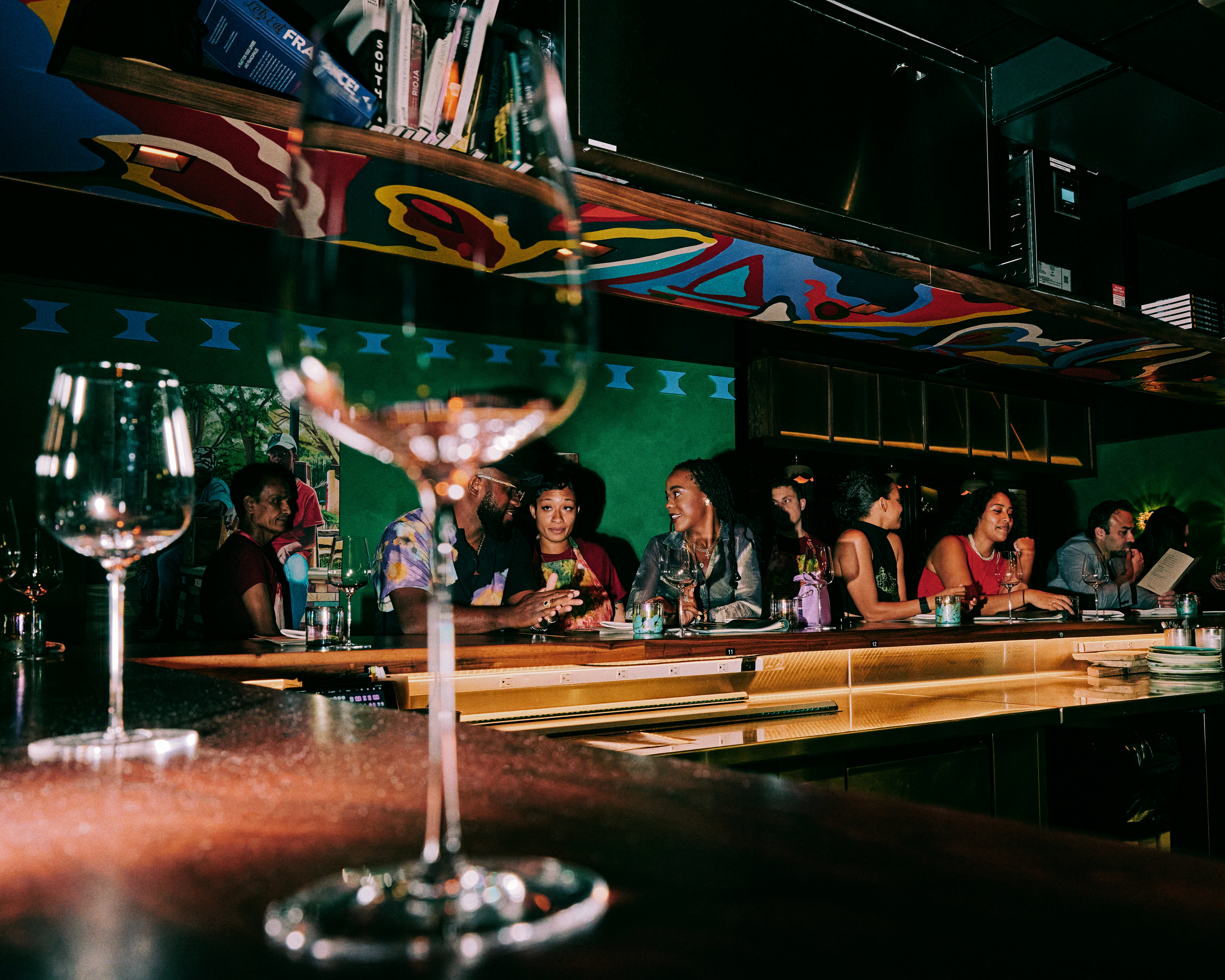 People sit at a wooden bar with a mural on the wall behind them.
