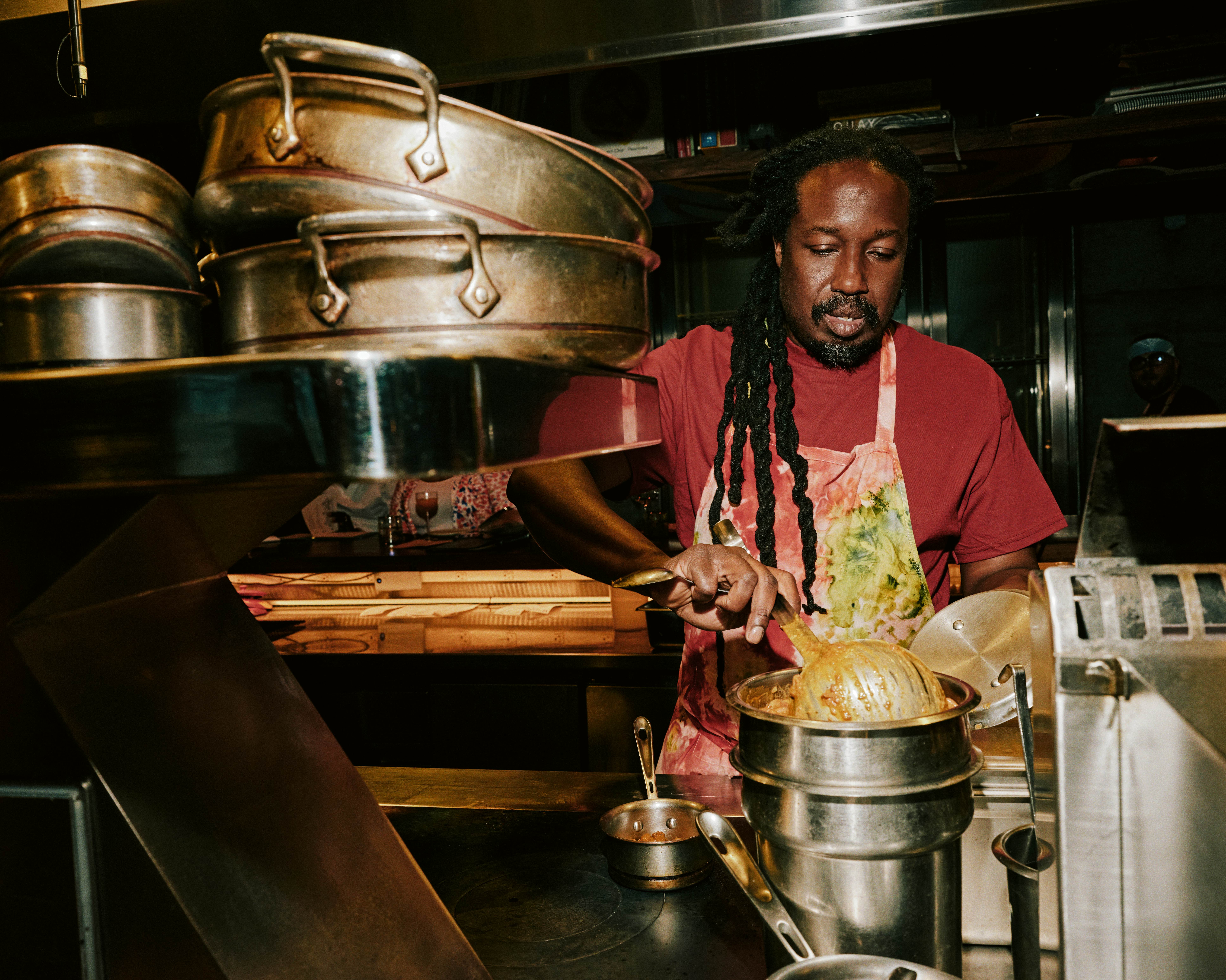 A man in a red T-shirt and tie-dye apron working in a restaurant kitchen.