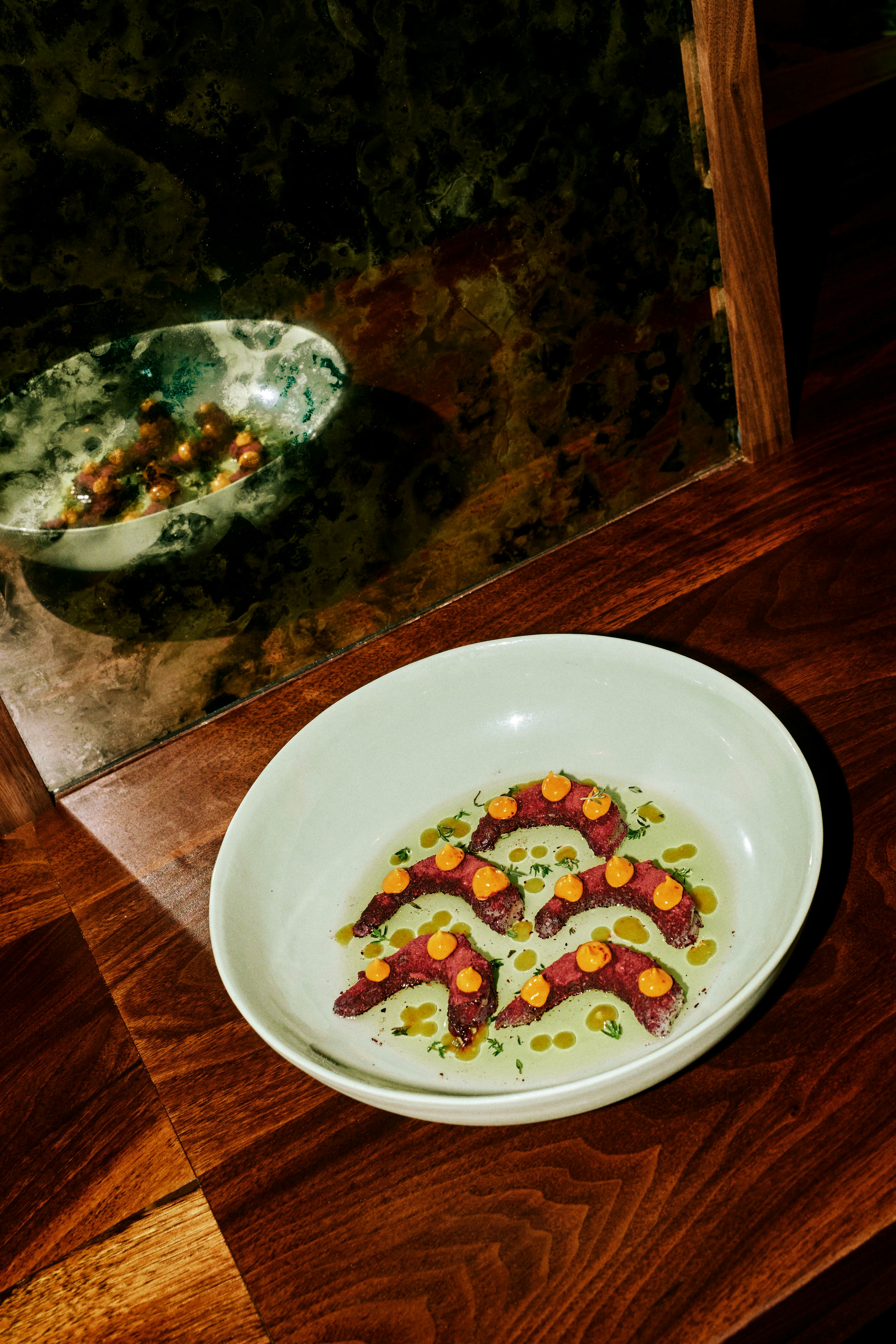 A white bowl with five shrimp topped with an orange sauce reflected in a mirror.