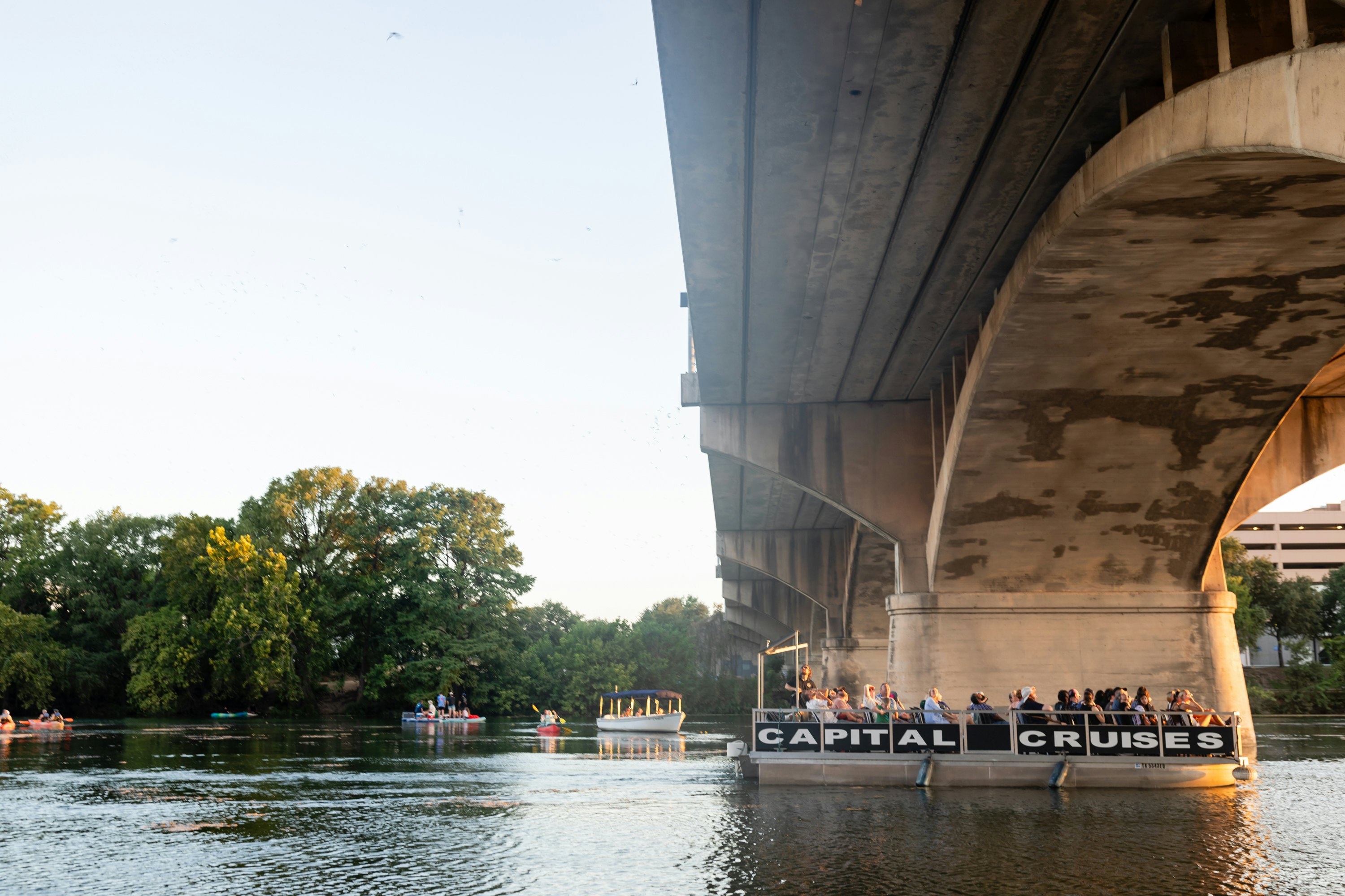 A boat with the words "Capital Cruises" on the side ferries passengers on a river under a bridge