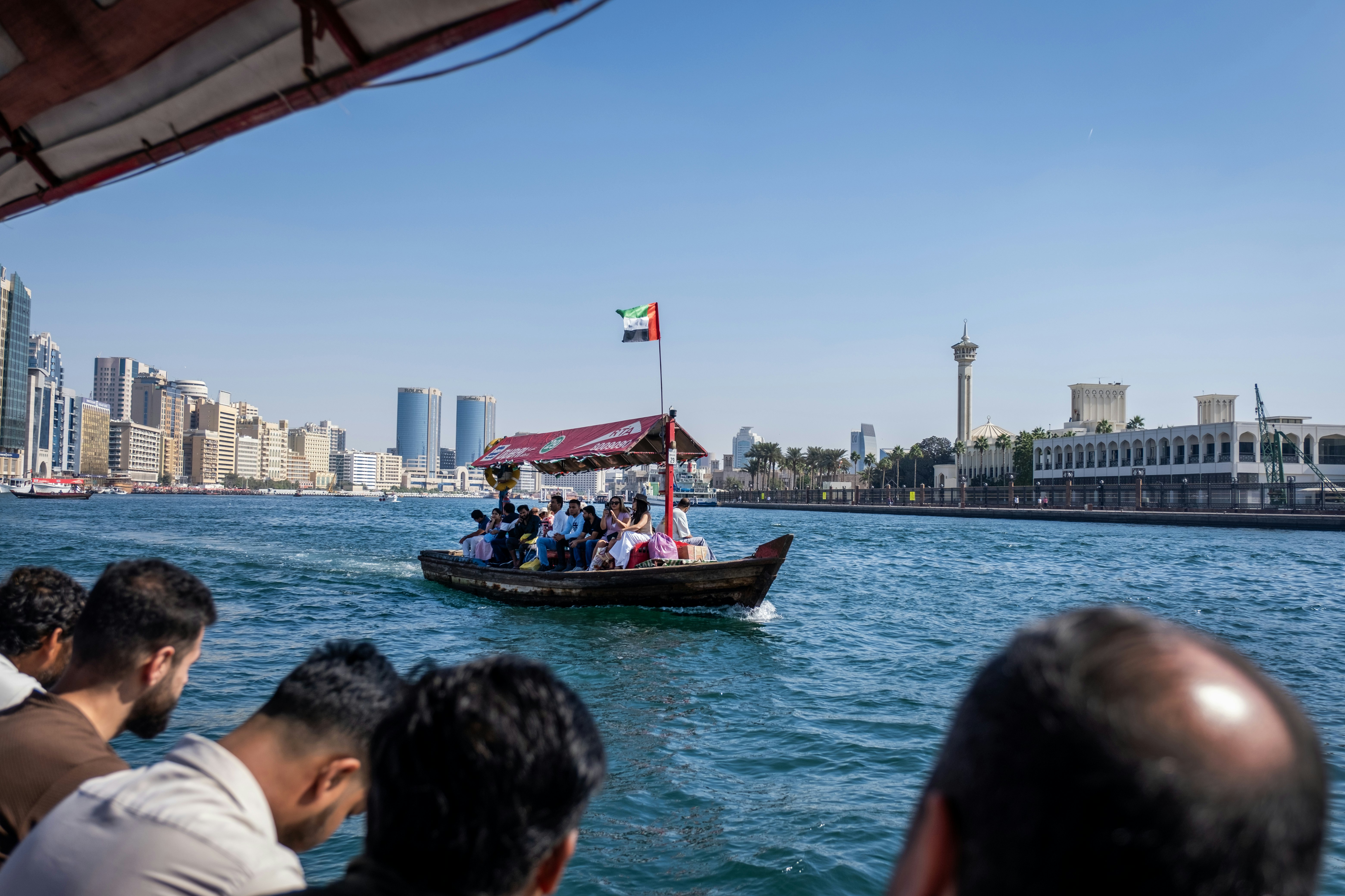 People look out onto the water as a boat crosses with a cityscape in the background
