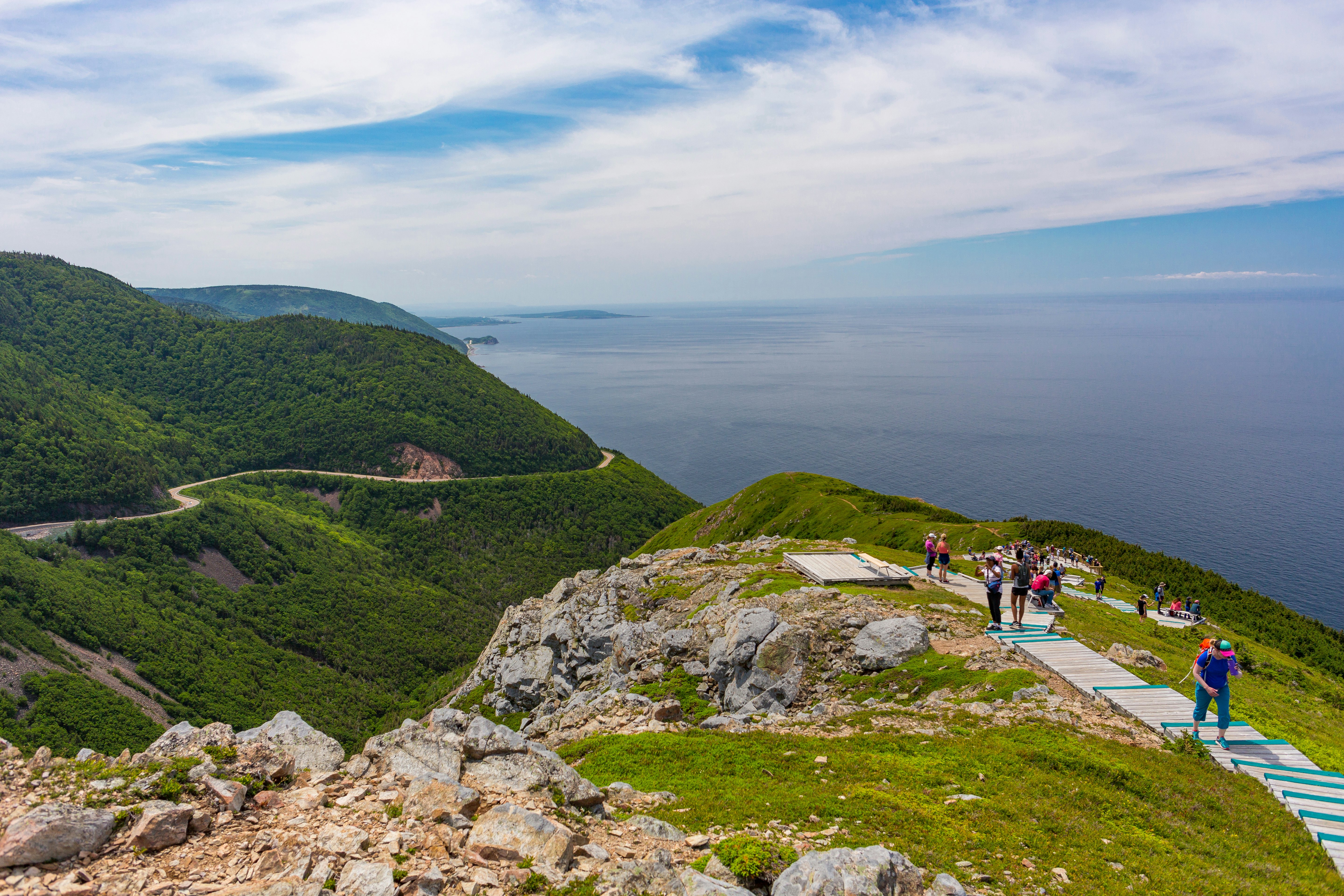 Hikers follow a boardwalk over the top of a cliff with extensive coastal views.