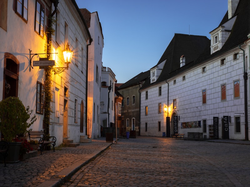 Cobblestone street with rowhouses on either side and lamps lit.