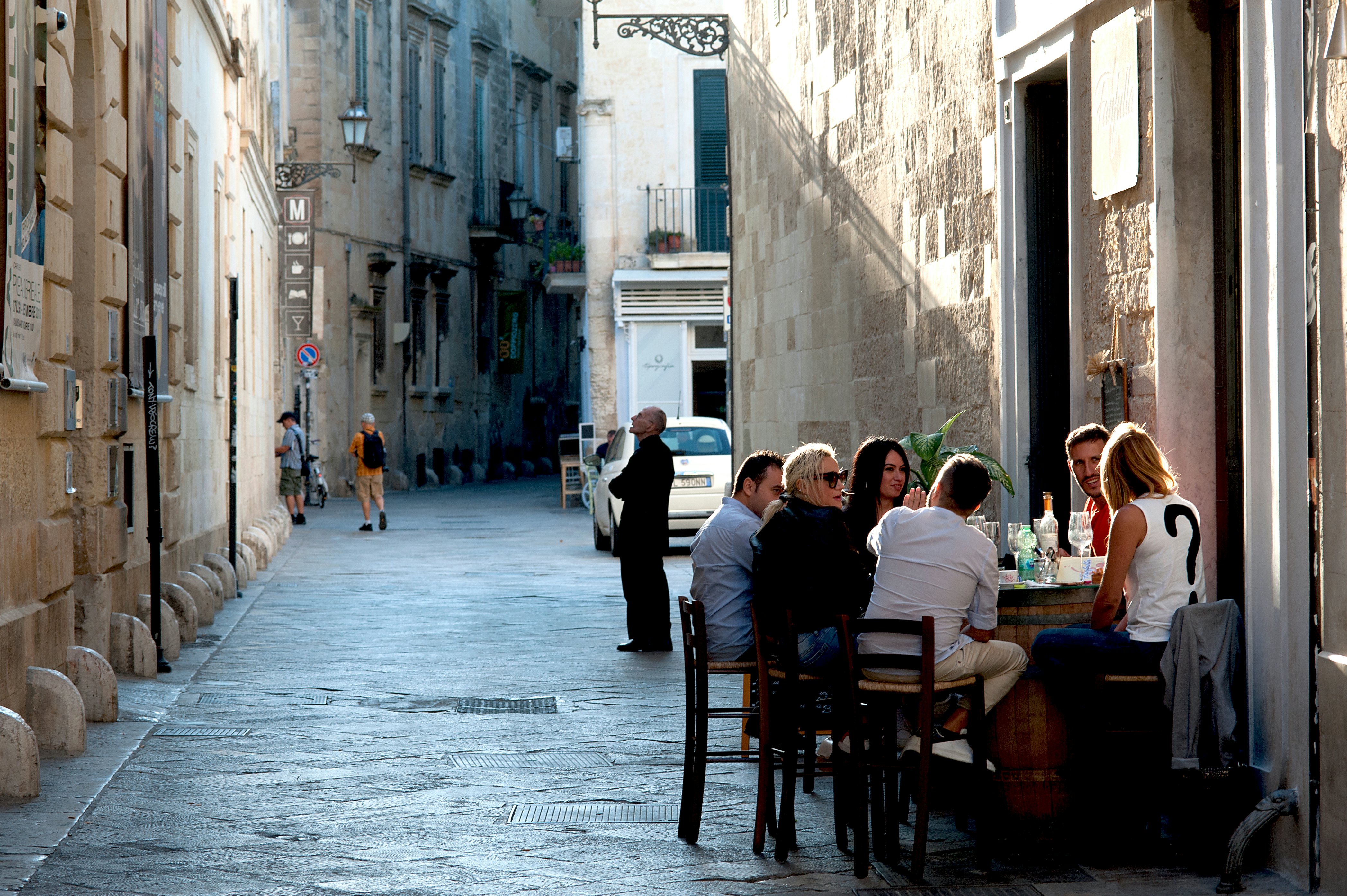 Friends enjoying a drink in a streetside cafe, all tightly packed around a barrel.