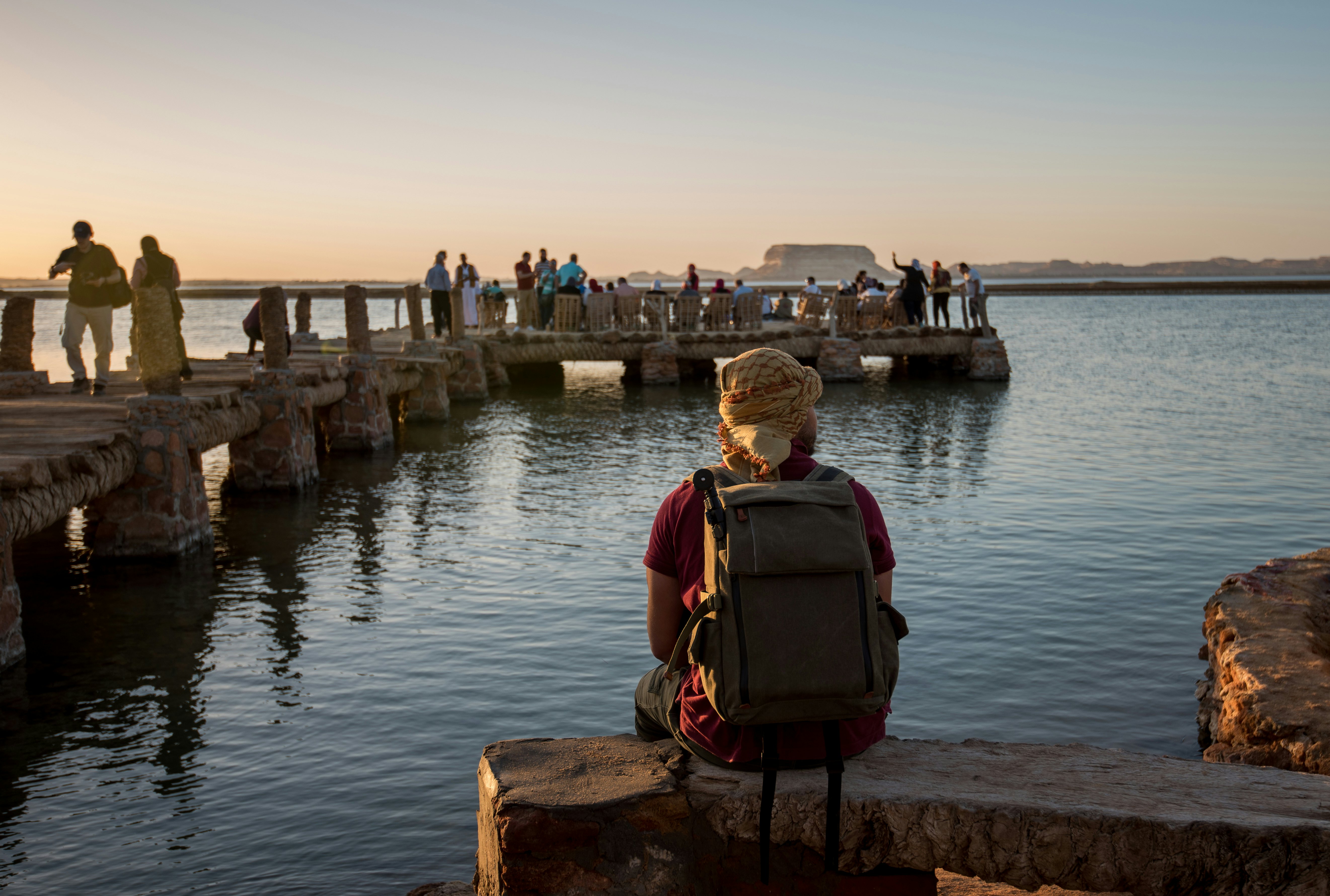 People standing or sitting on a dock over water as the sun sets