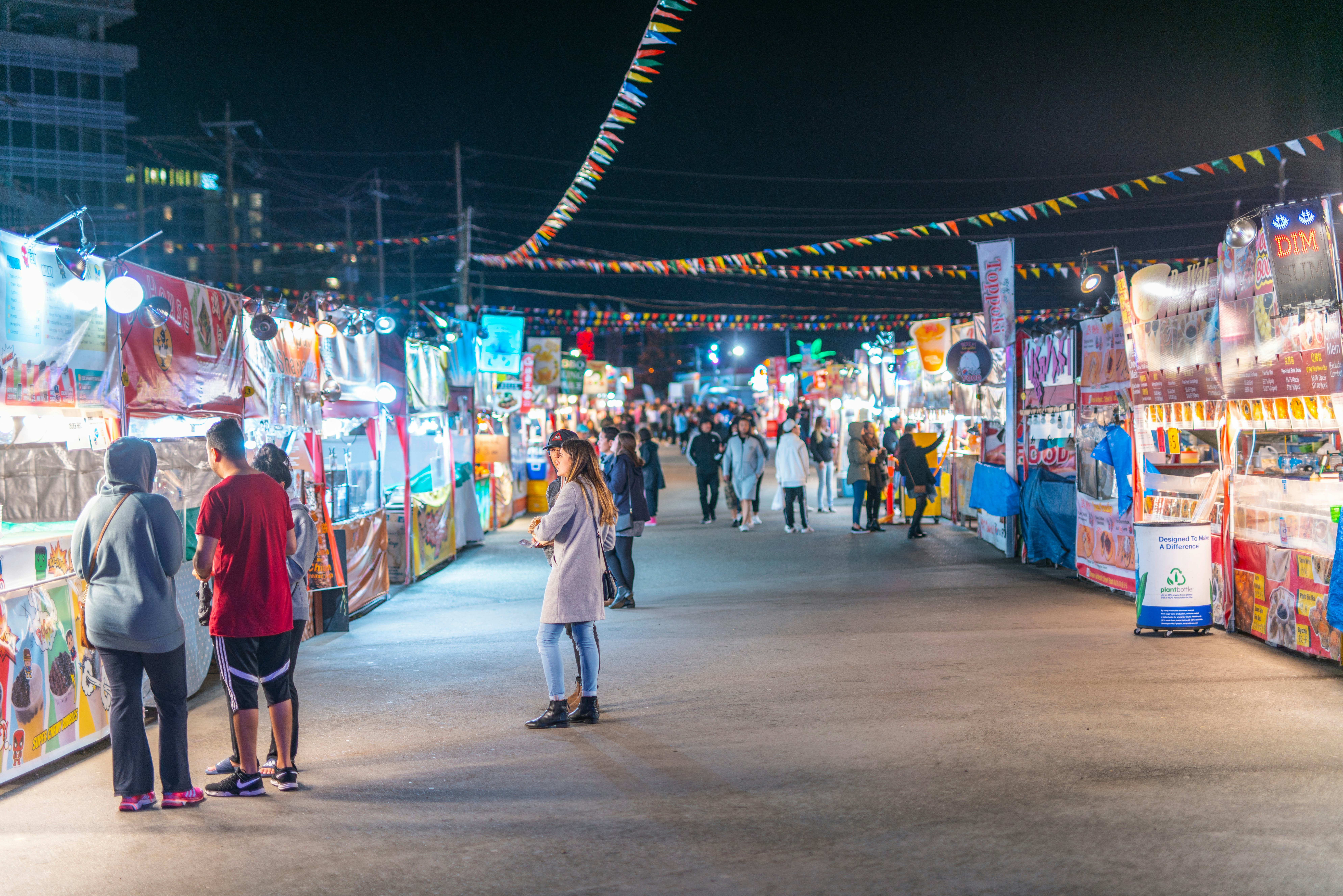 People shopping at the colorful food stores full of colorful lights at night.