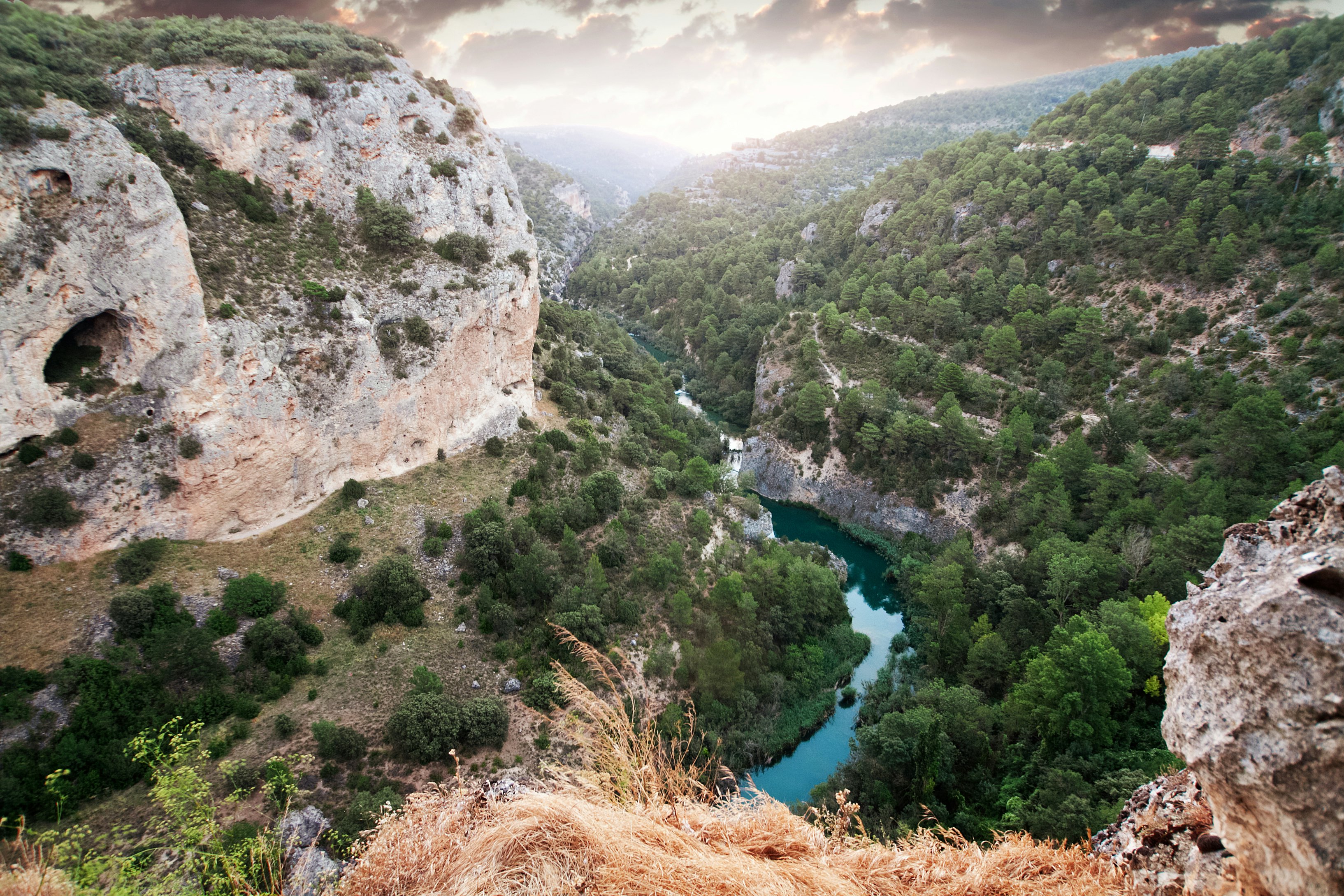 View from a cliff top of the Río Júca cutting through the Ventano del Diablo canyon with a hazy sky above.