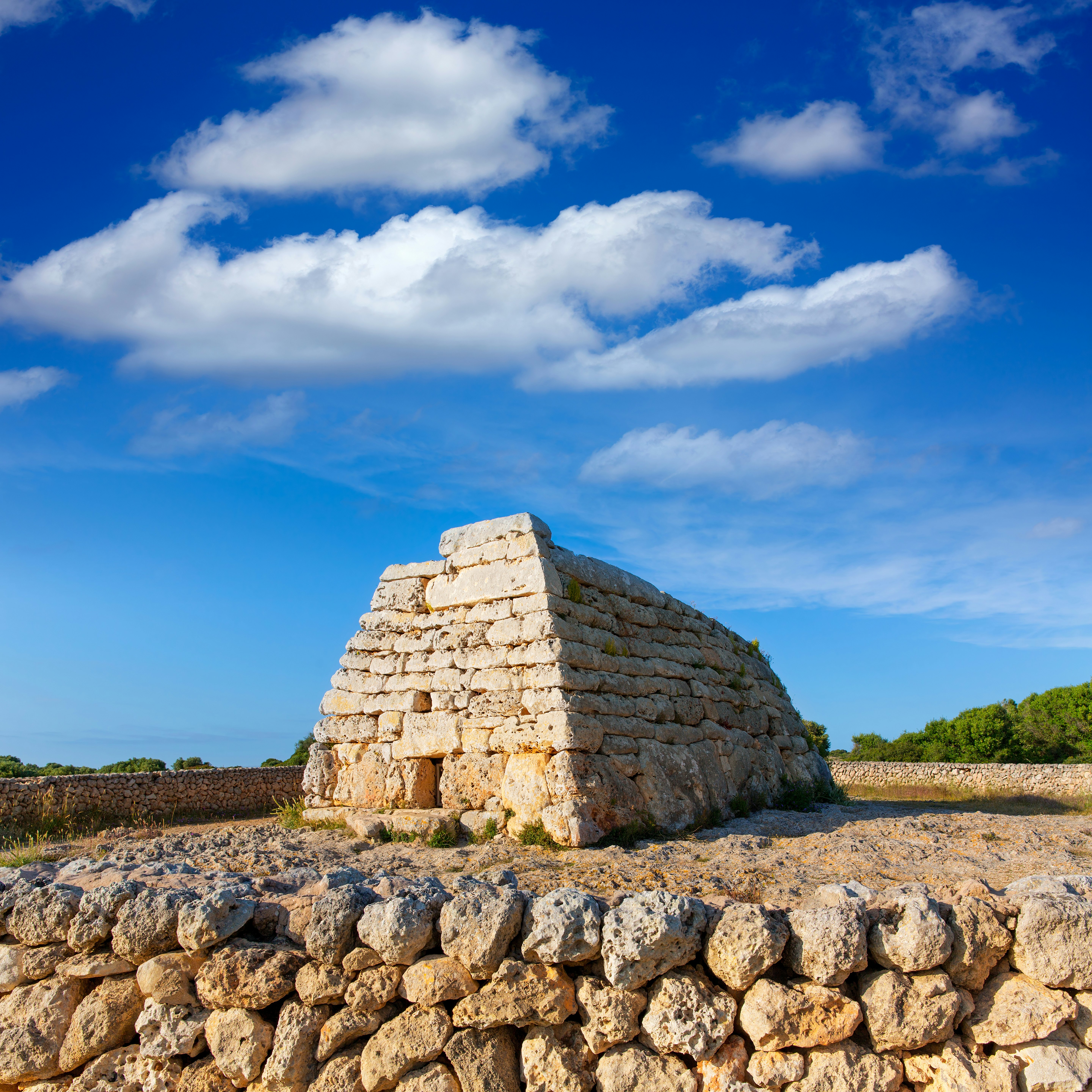 Menorca Ciutadella Naveta des Tudons megalithic chamber tomb In Balearic islands with a sunny blue sky above.