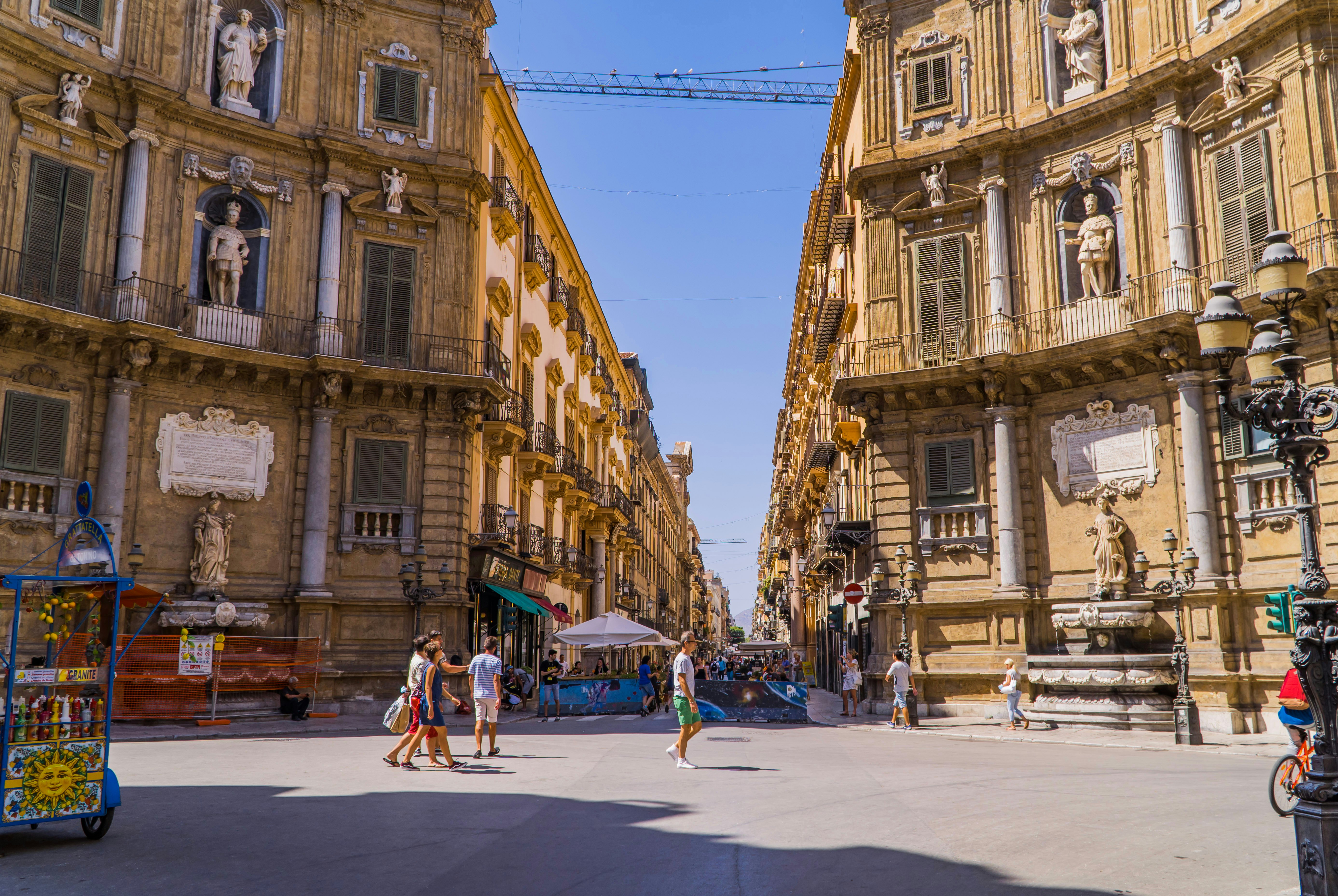 Tourists walking in front of the grand facades of the Quattro Canti in Palermo, Sicily.