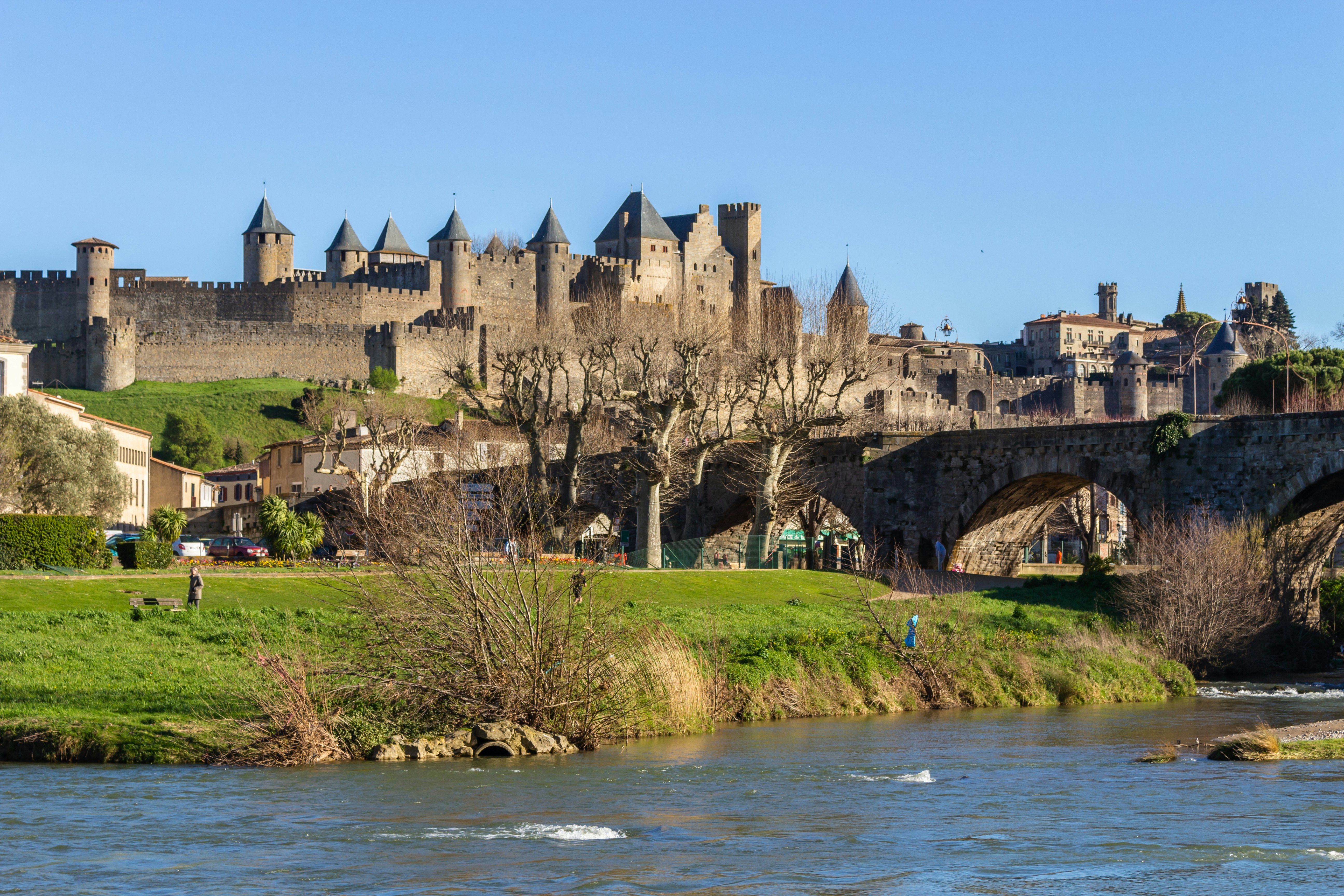 A stone bridge crosses a river leading to a vast fortified castle.