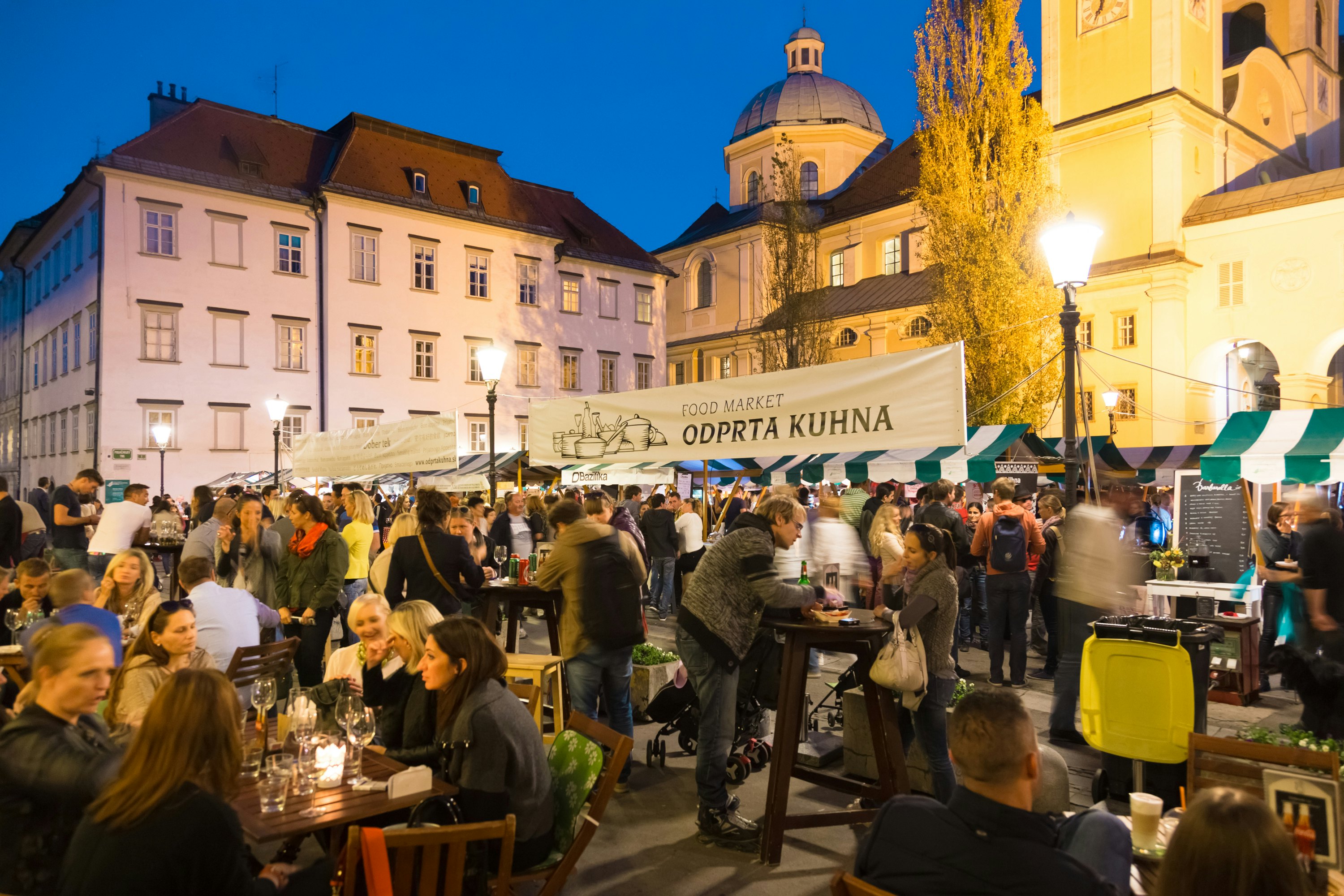 People dine at tables beside food stalls at an open-air culinary night market.