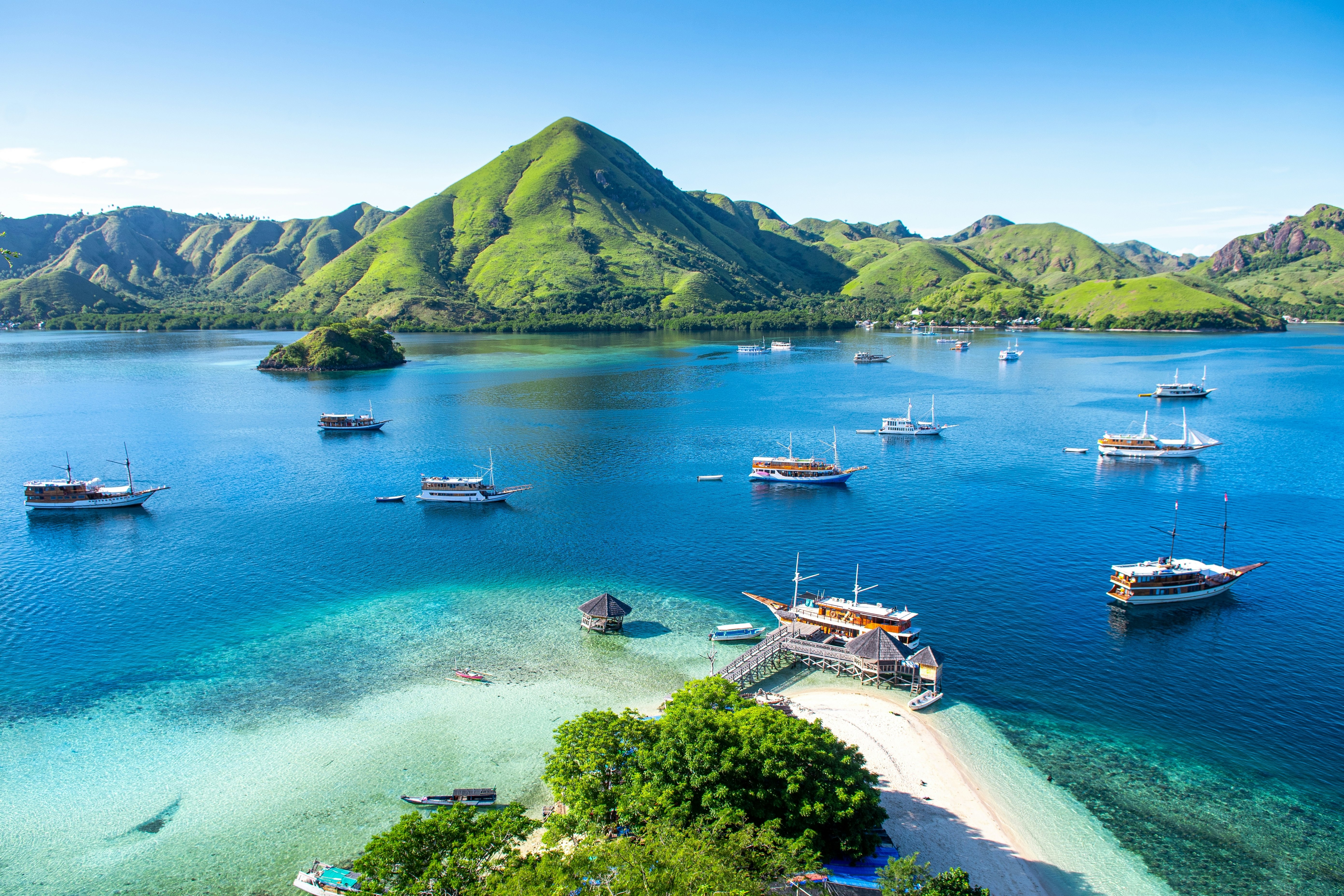 Boats moored in the blue bay between islands covered in green foliage.
