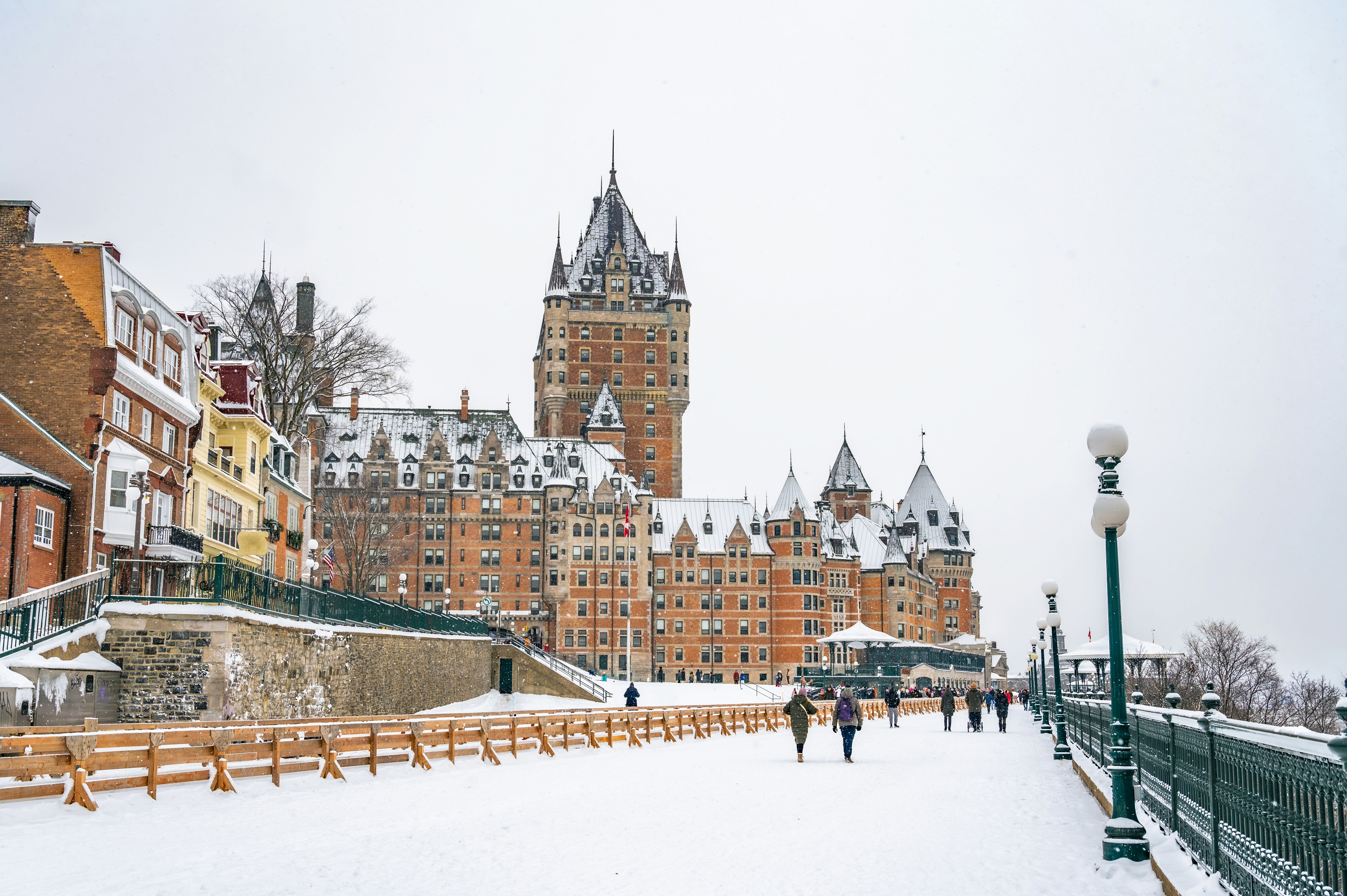 People walk on a snowy promenade toward a redbrick building with many turrets.
