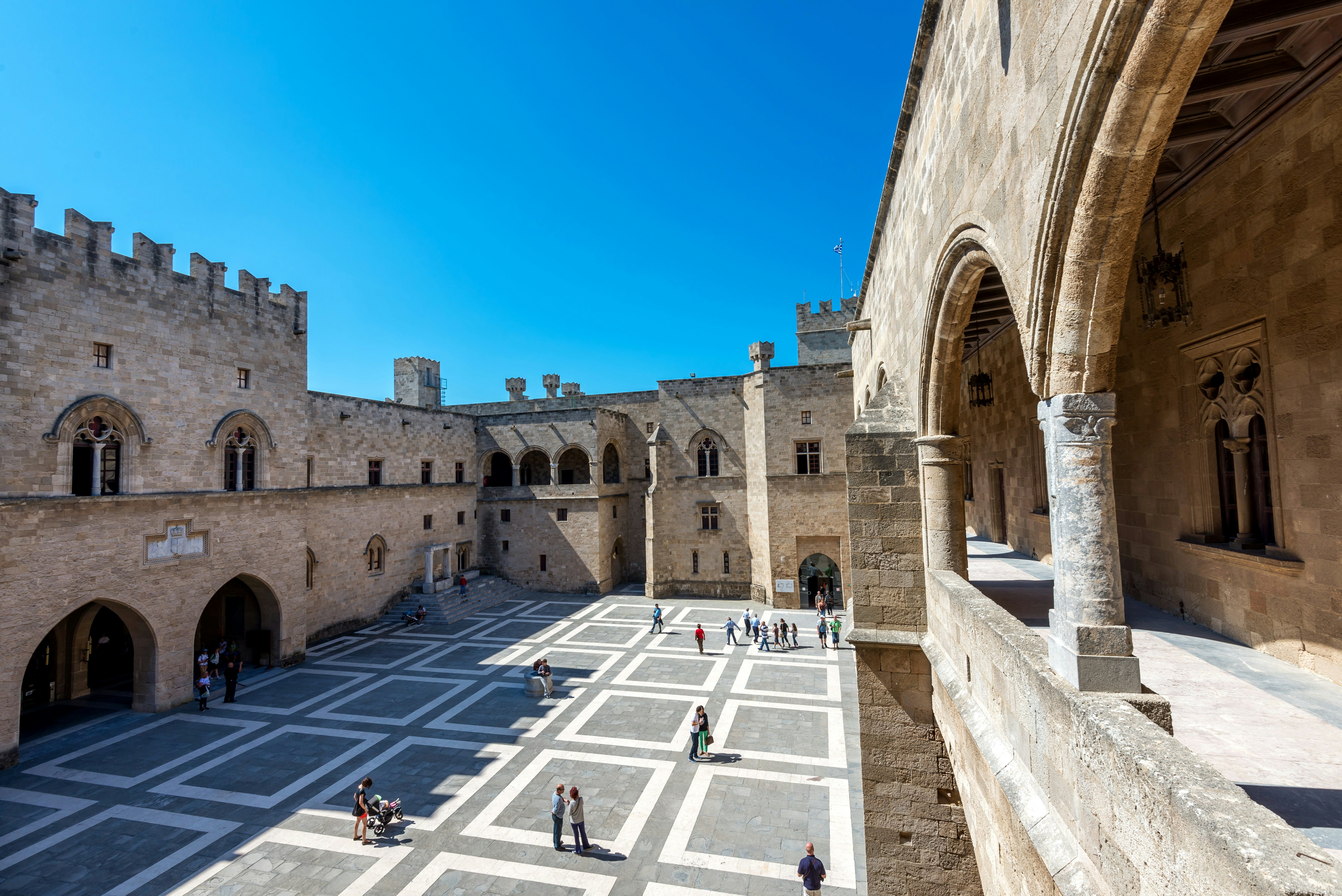 A wide view of people standing in the courtyard of a medieval palace in a city.