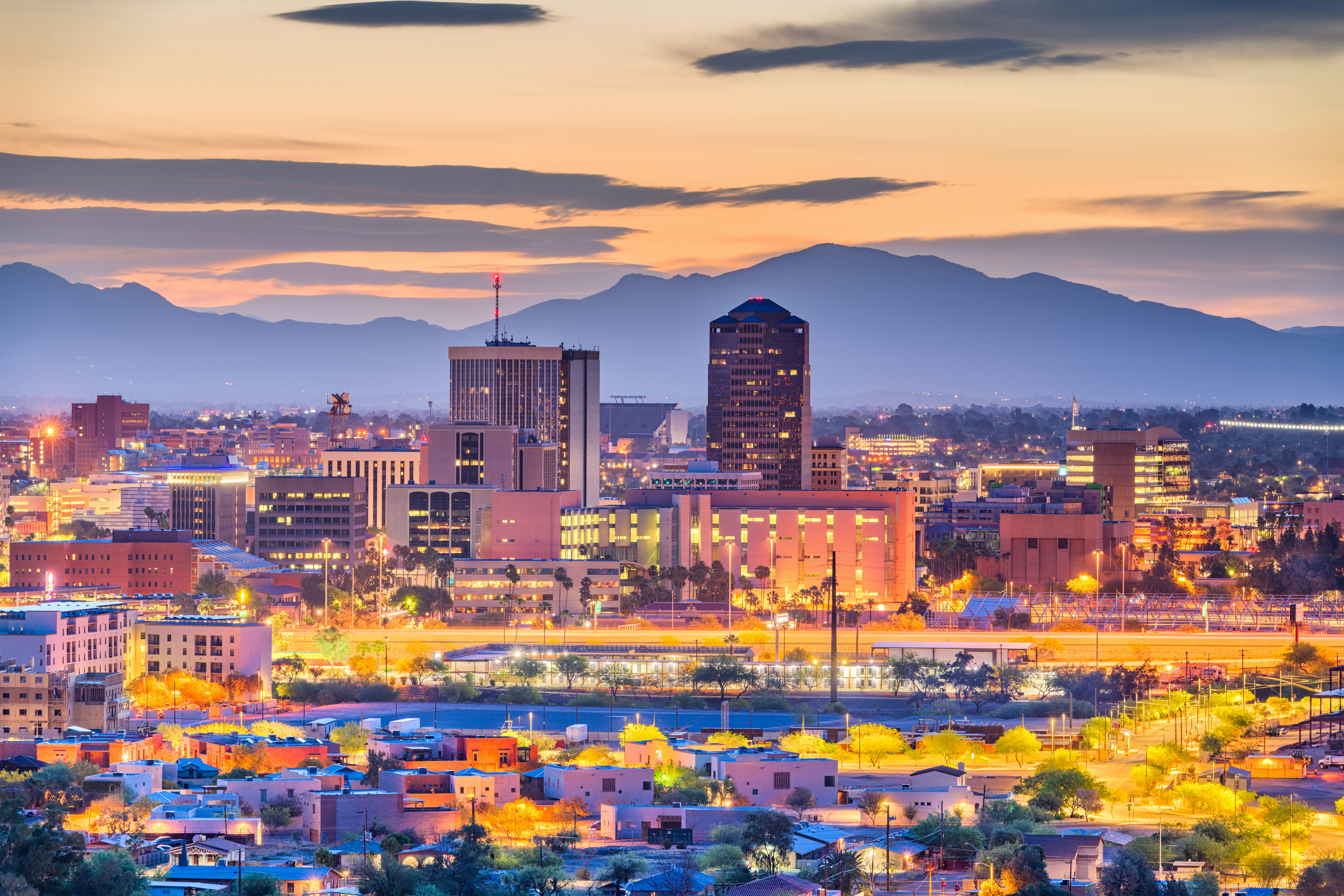A city glowing with yellow light at dusk. Moutains rise in the distance.