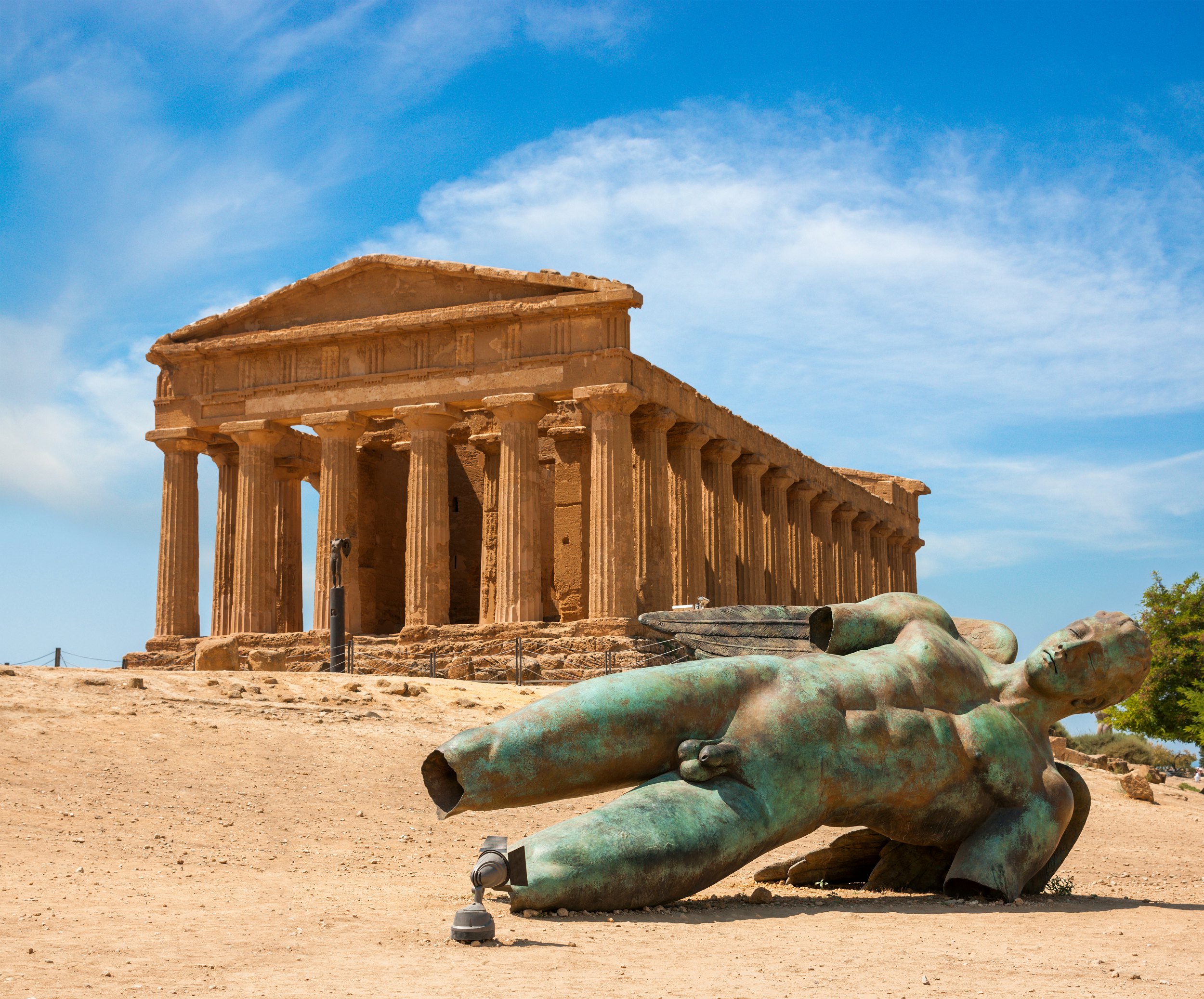 A fallen bronze statue in front of the ruins of a temple.