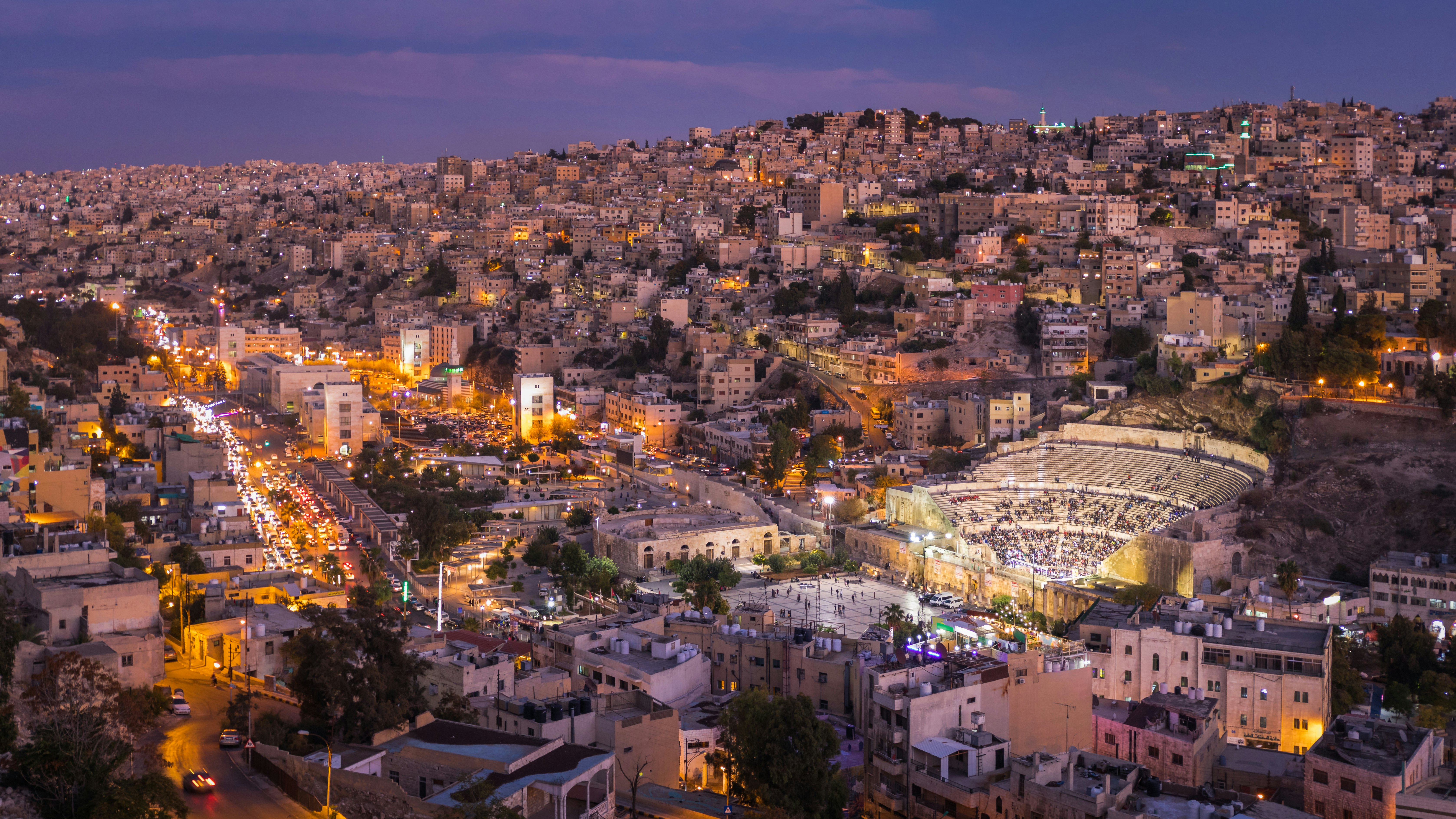 A large amphitheater, with people on seats, in the center of a hilly neighborhood at dusk.
