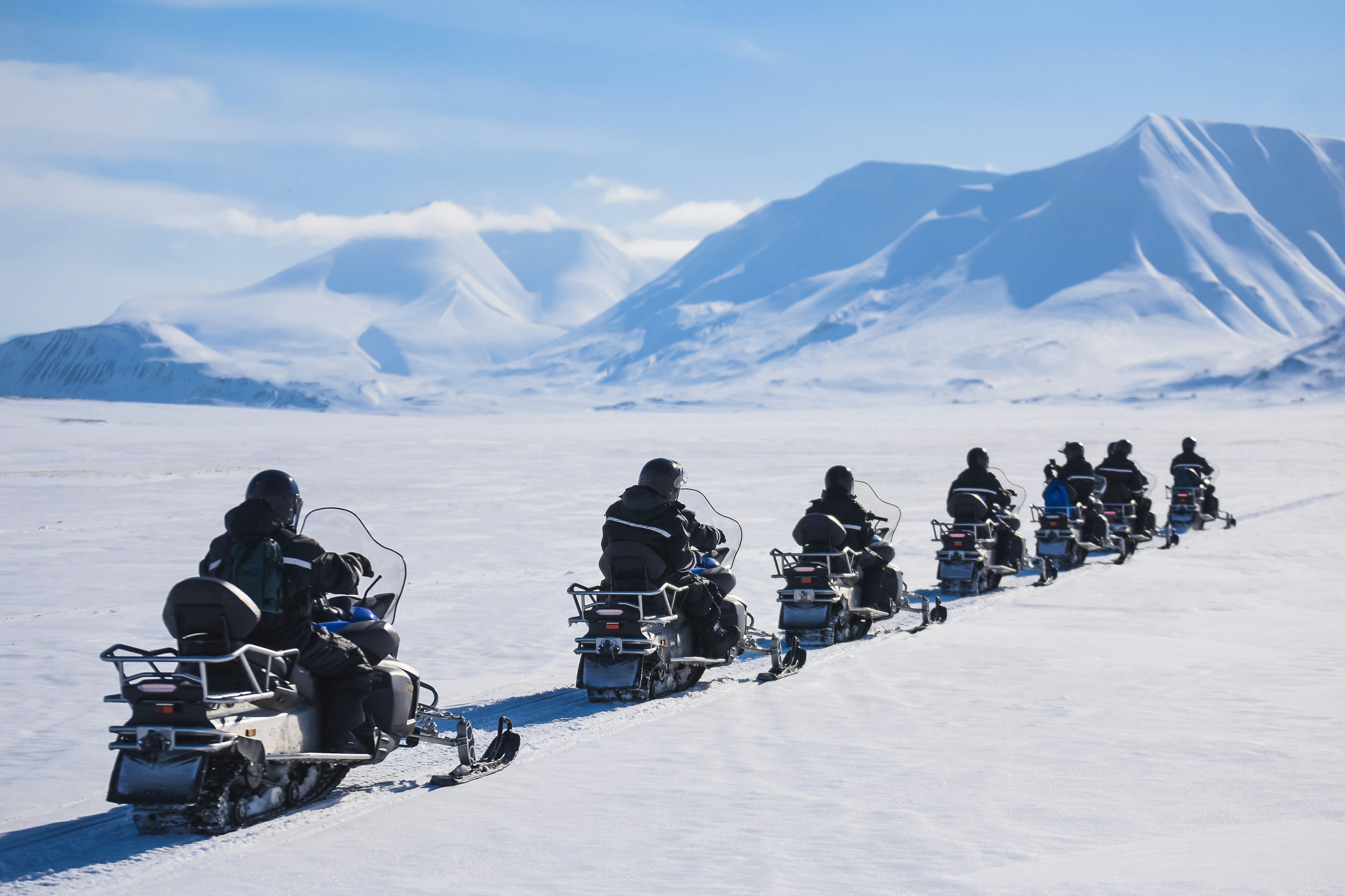 A row of people on snowmobiles in the icy landscape of Svalbard