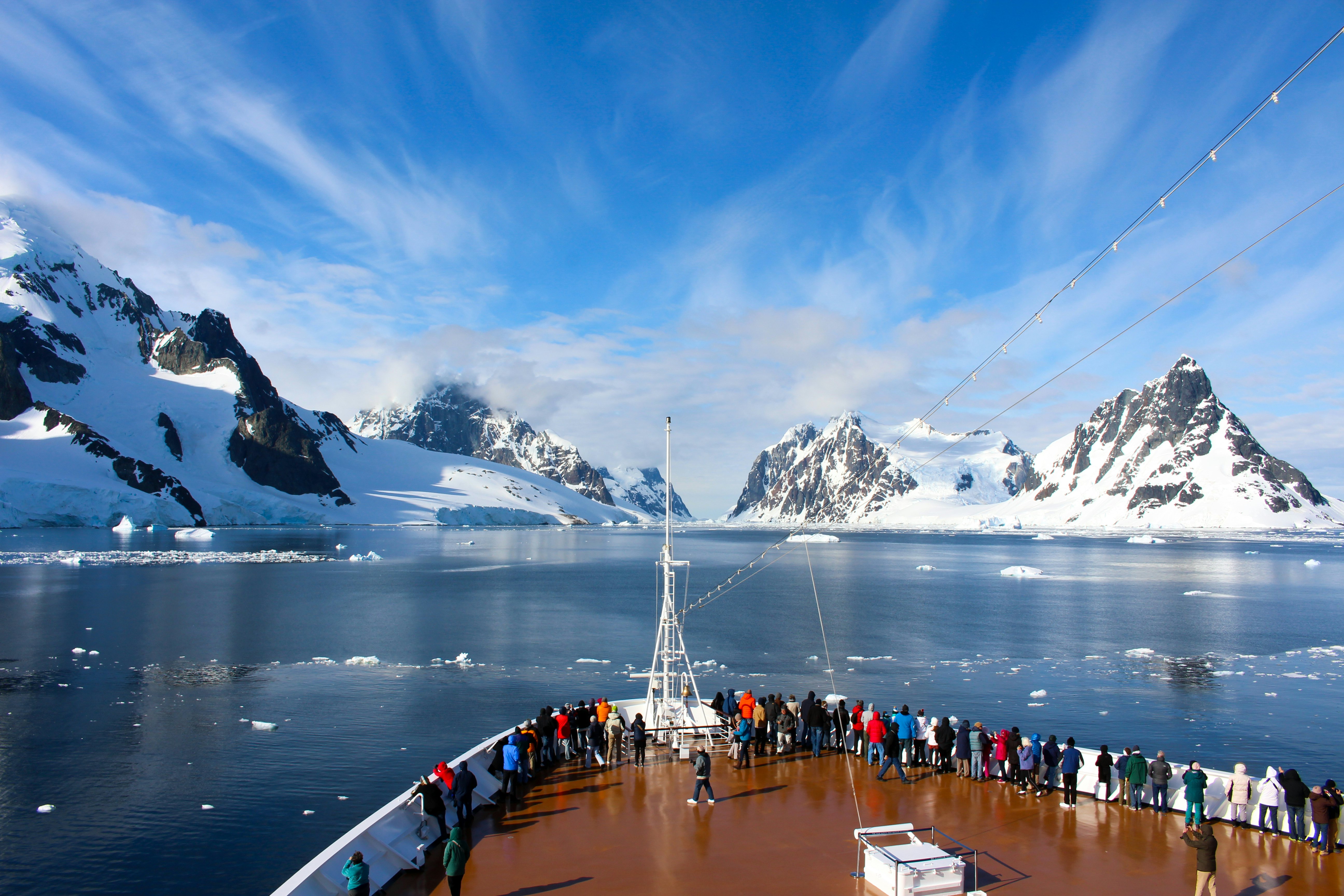 Passengers on deck on a cruise ship passing a rocky coastline in the Antarctic Peninsula.