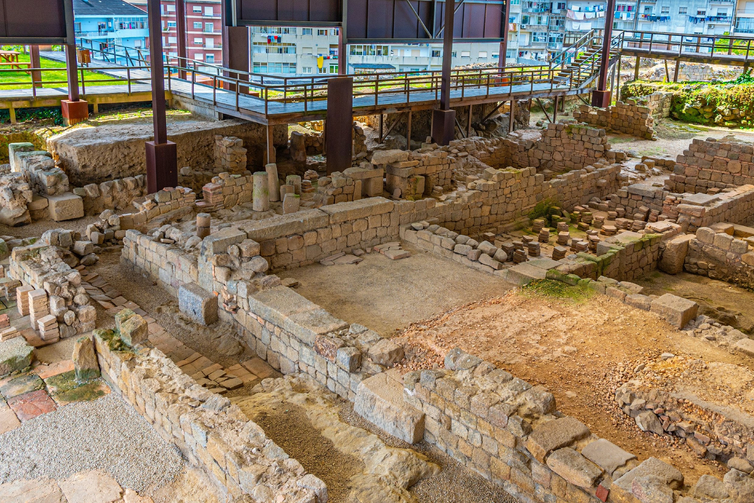 An archeological site in Portugal is seen from above, revealing walls and columns; it is covered by a roof and has raised walkways around the far perimeter.
