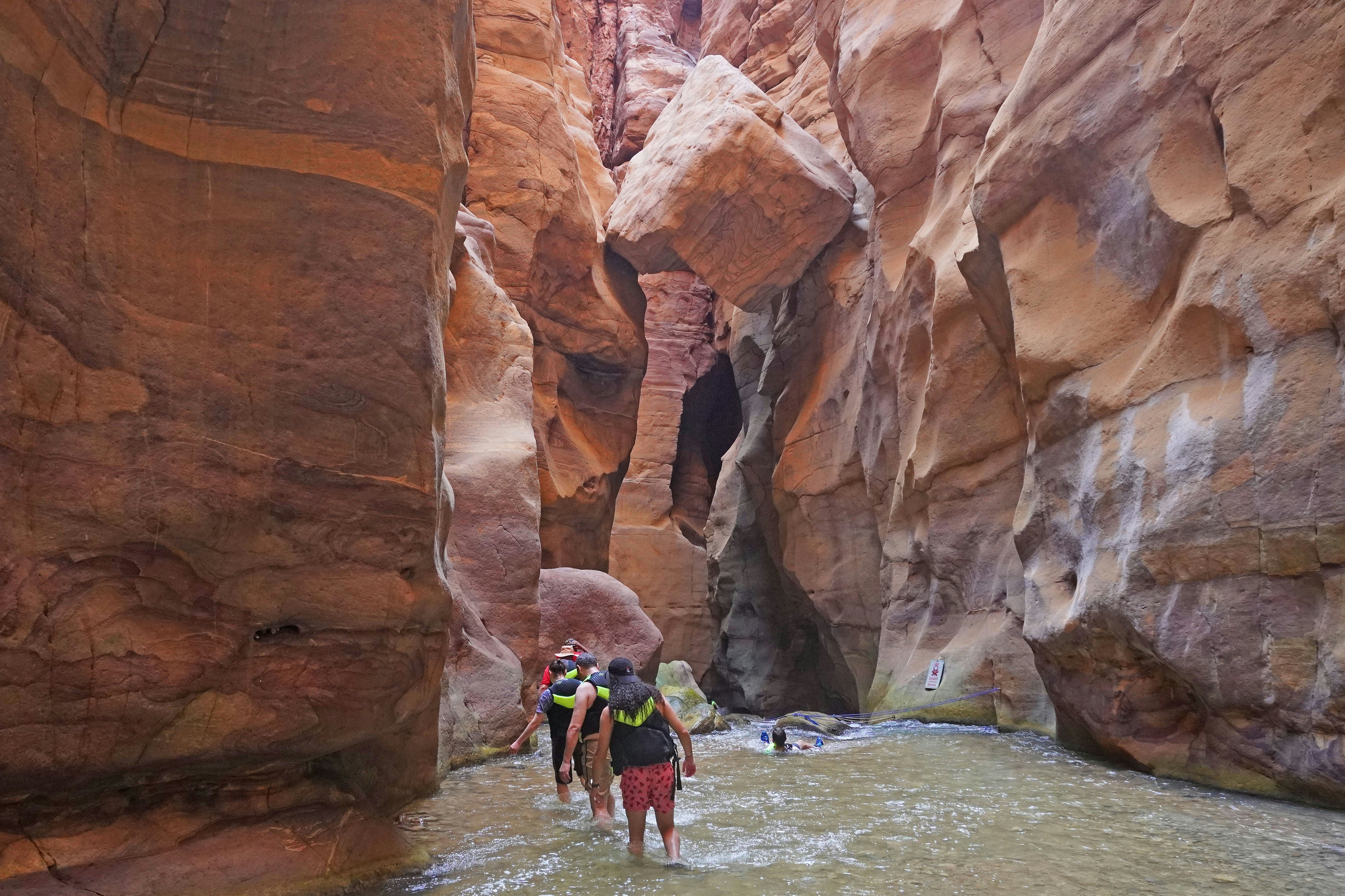 A small group wades through a stream running between steep canyon walls.