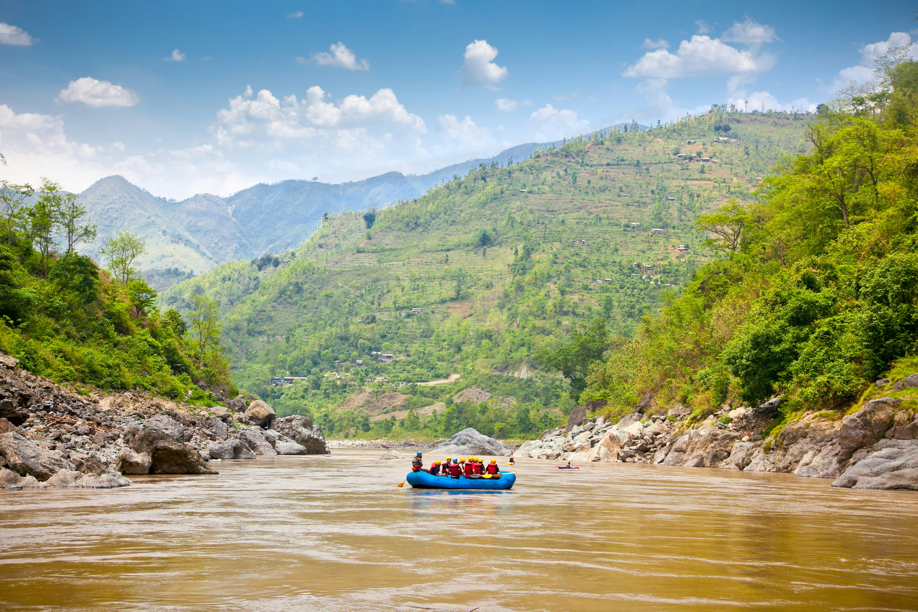 A raft loaded with people sets sail on a river with steep valley sides.