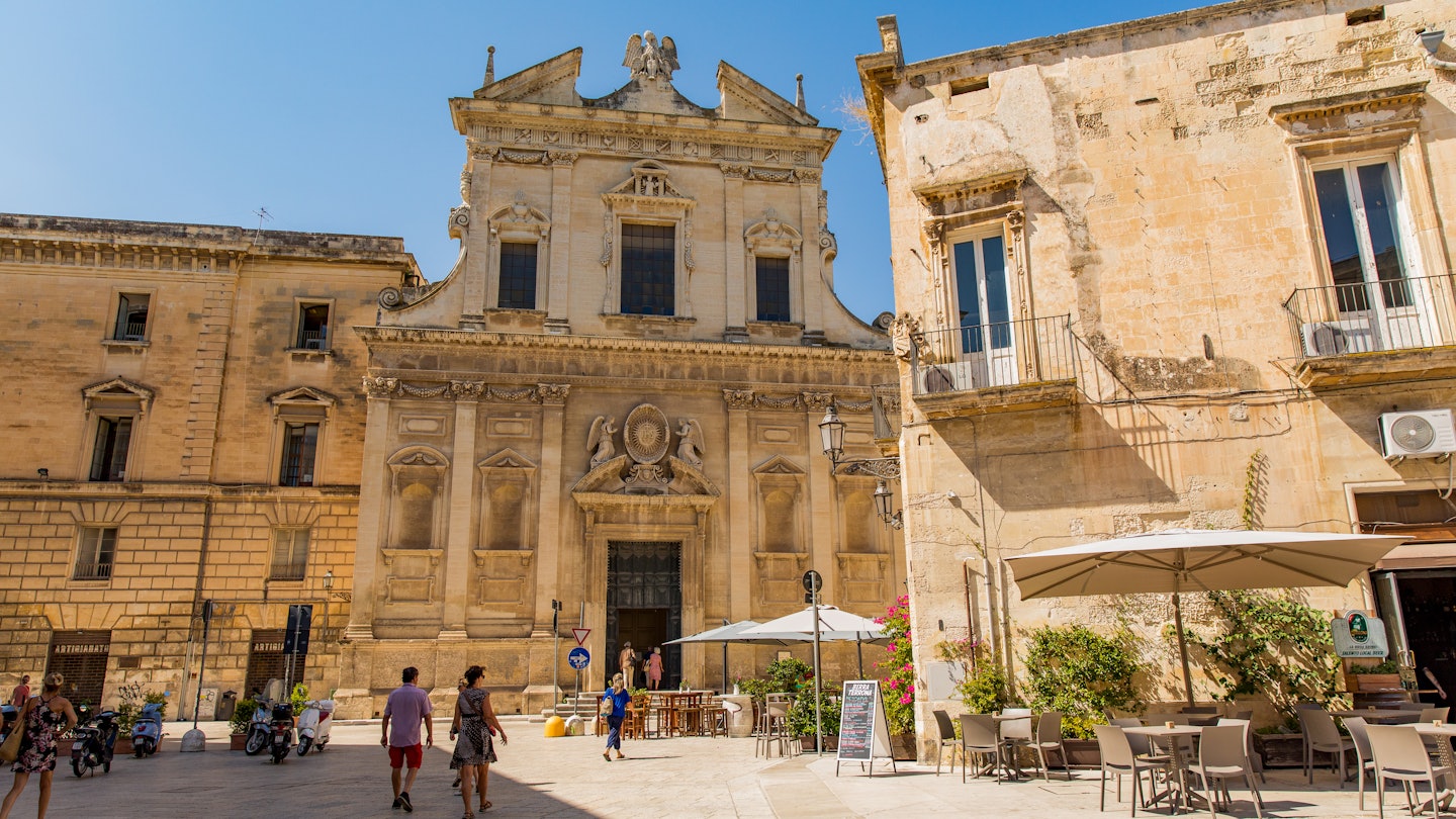 People passing a baroque church on a square in Lecce, Italy.
