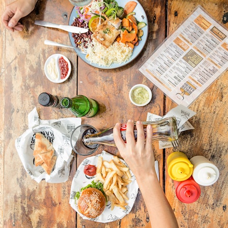 Two people sit at a wooden table eating a salad and a burger with fries.