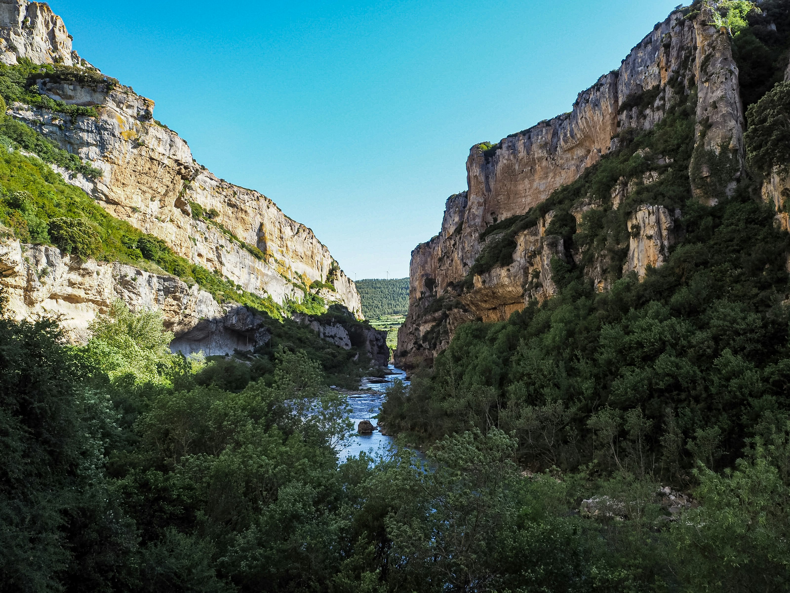 A river flows past walls and grottos in a canyon.